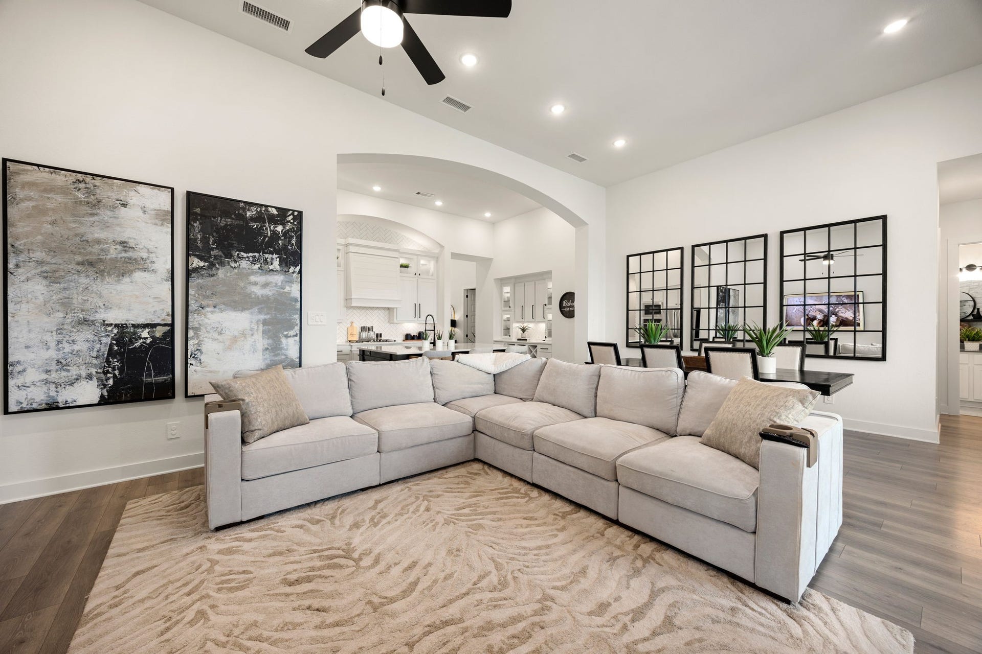 31322 Crescent Hill Drive, Fulshear, TX 77441 Designed for effortless modern living. This vast main room showcases stunning wide-plank flooring, crisp white walls, recessed lighting, and a grand arched opening that frames a bright view into the adjacent kitchen and dining spaces.