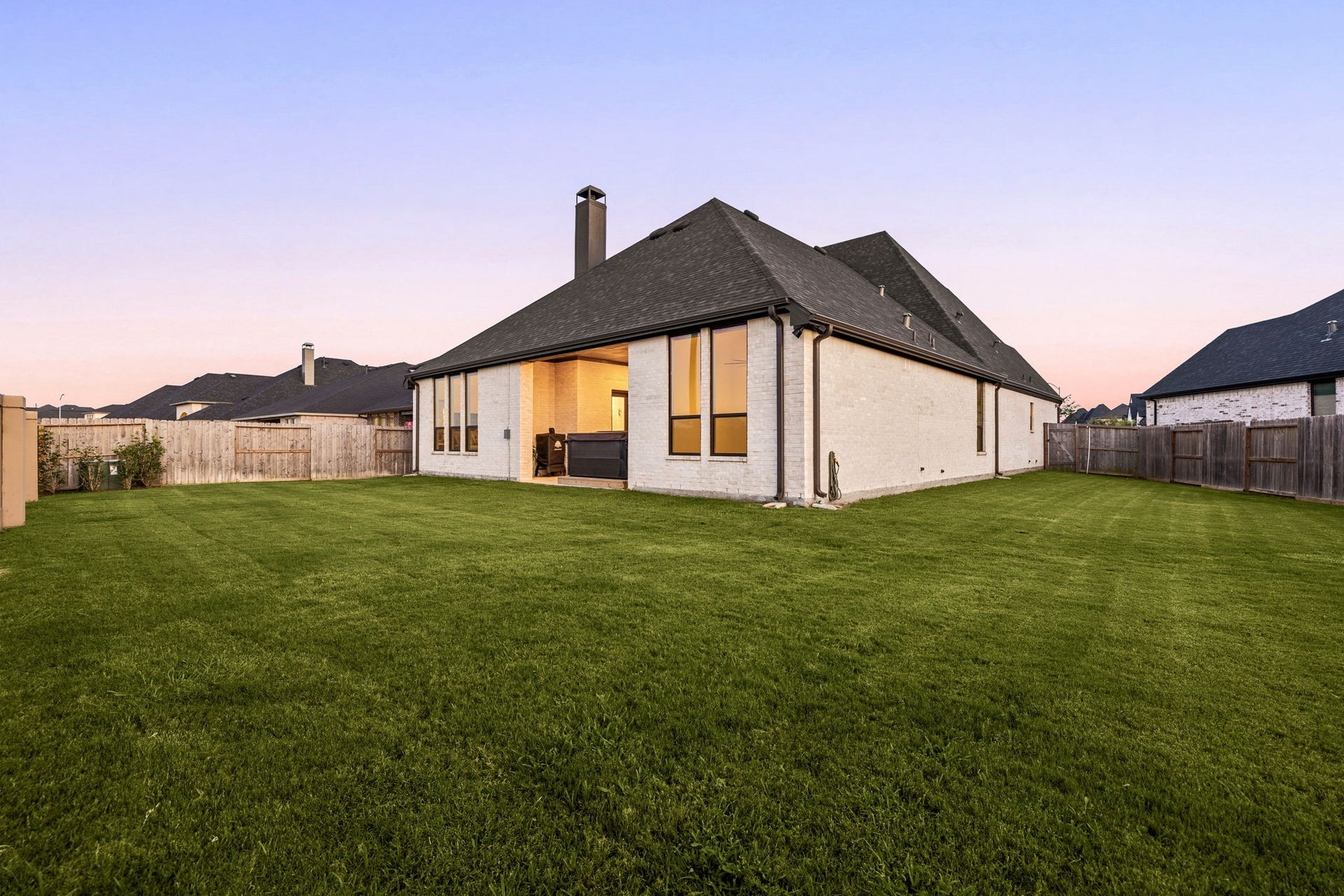 31322 Crescent Hill Drive, Fulshear, TX 77441 An expansive, fully fenced backyard. A wide stretch of lush green lawn offers endless possibilities for outdoor activities, framed by a complete wooden privacy fence, a sleek brick chimney profile, and a covered back patio area.