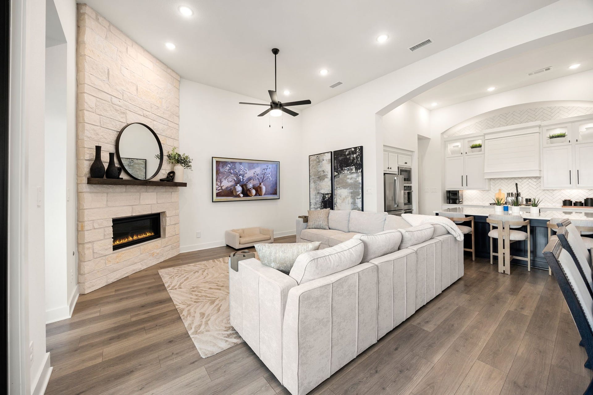 31322 Crescent Hill Drive, Fulshear, TX 77441 The ultimate open-concept design. High-end wide-plank flooring connects the bright living room to the adjacent kitchen, highlighted by a modern linear stone fireplace, recessed ceiling lights, and an arched architectural walkthrough.