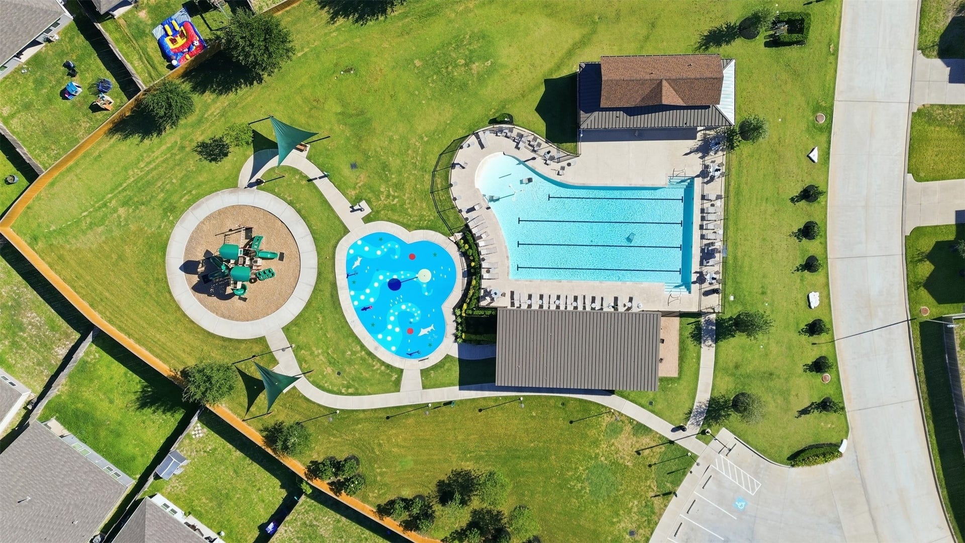 Discover a vibrant community space featuring a large pool with lap lanes, a playful splash pad, and a well-equipped playground, all surrounded by lush green lawns and shaded seating areas.