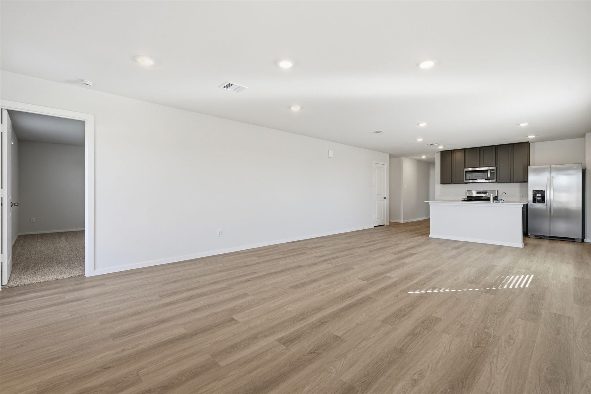 Spacious open-concept living area with sleek wood flooring and a modern kitchen featuring stainless steel appliances and dark cabinetry.