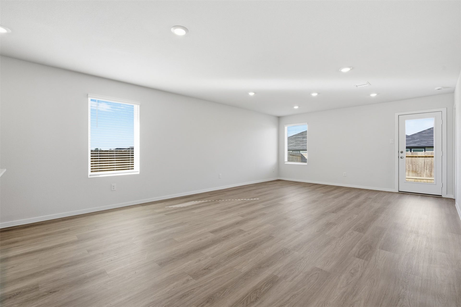 Spacious and bright living area with sleek hardwood floors, recessed lighting, and ample natural light through large windows, offering a modern and inviting atmosphere.