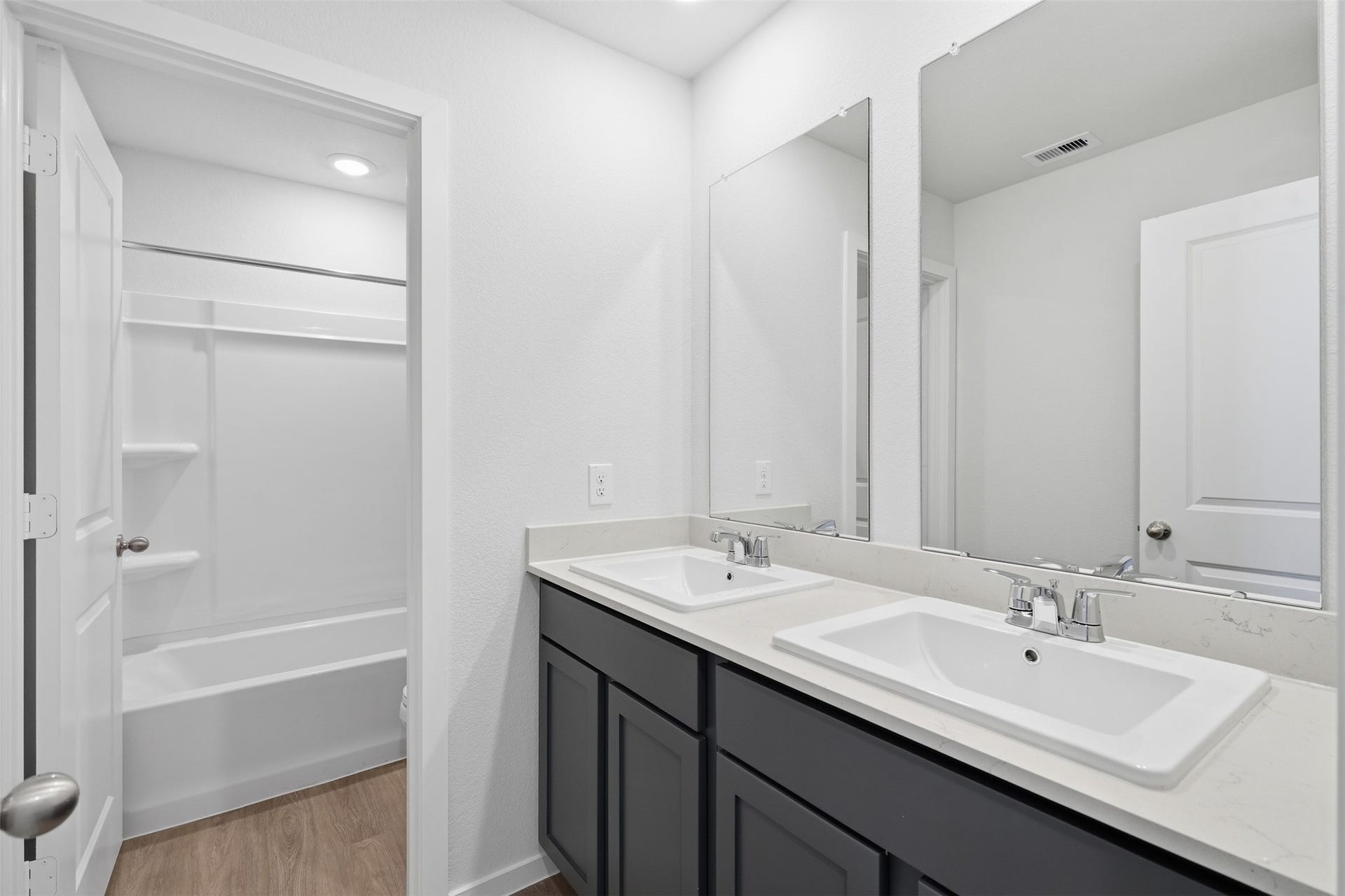 Modern bathroom featuring dual sinks with sleek fixtures, spacious vanity mirrors, and a separate bathtub area with a contemporary design.
