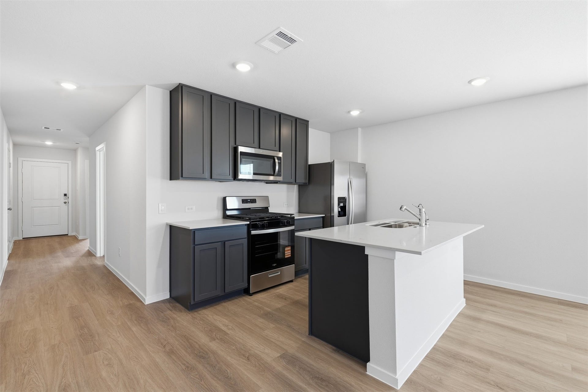 Modern kitchen with sleek dark cabinetry, stainless steel appliances, and a spacious island. Bright, open layout with wood style flooring and ample natural light.