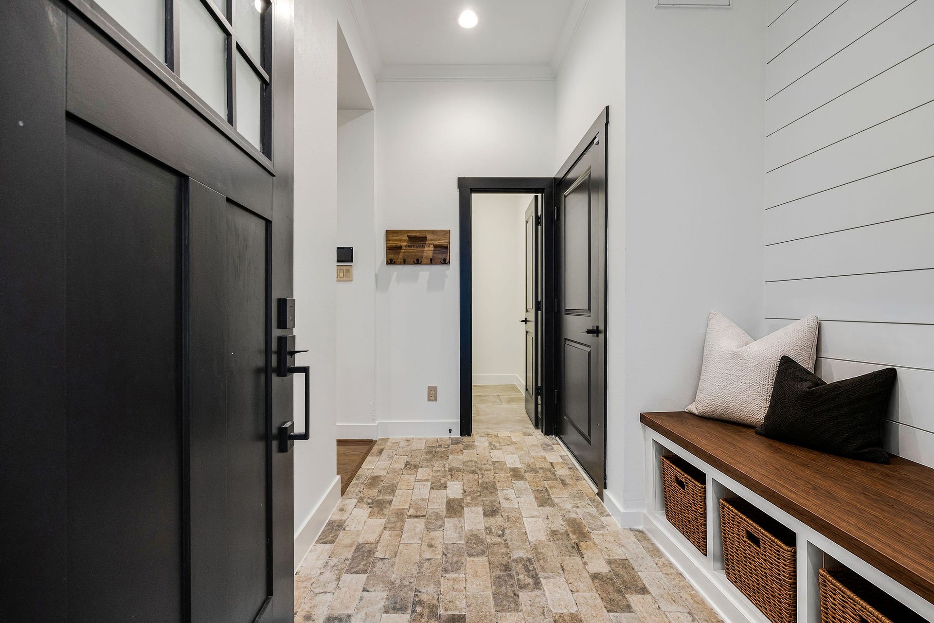 5537 Petty Street, Houston, TX 77007 This bright entryway featuring a stylish black door, brick flooring, and a cozy bench with storage baskets, complemented by a modern shiplap accent wall.