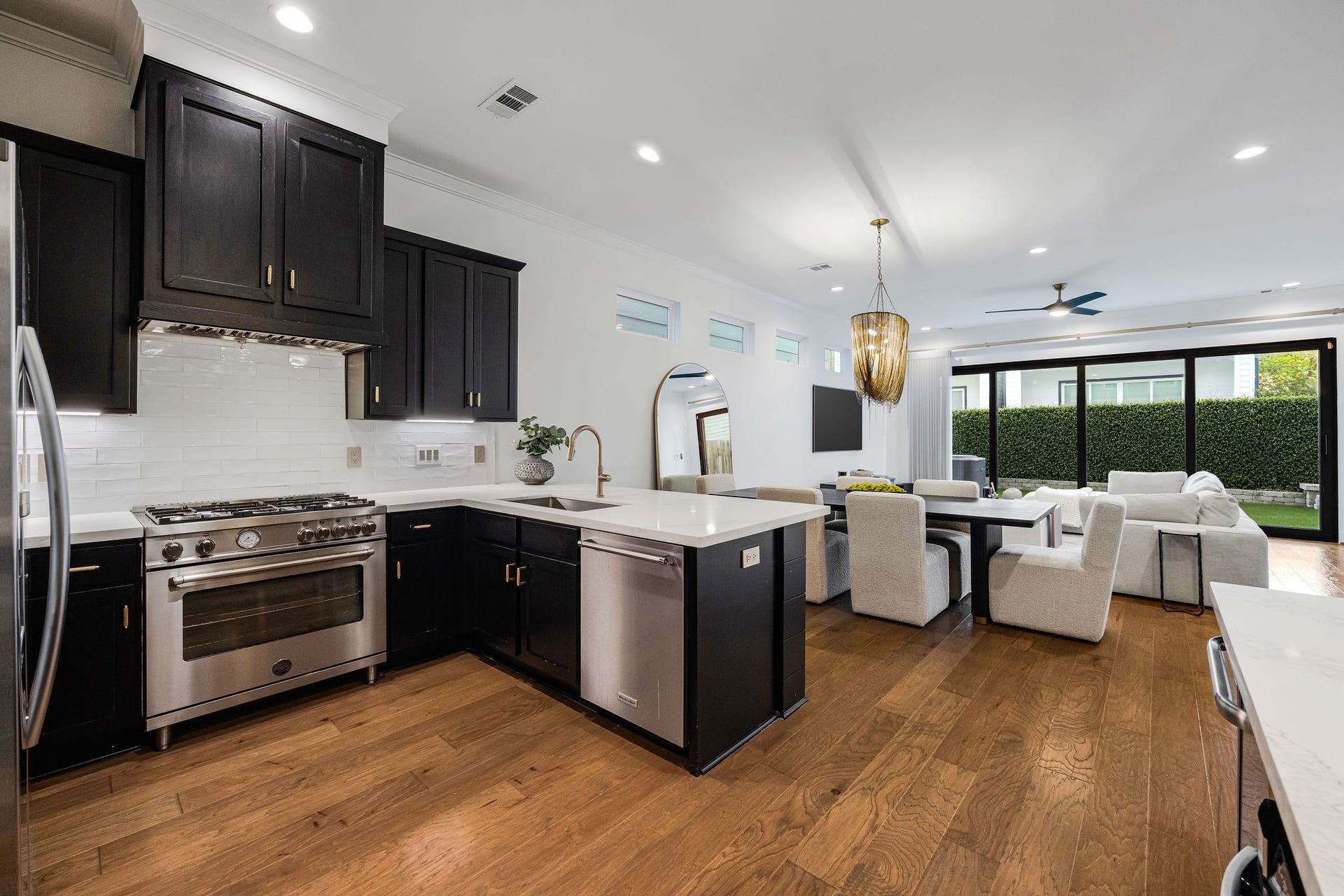 5537 Petty Street, Houston, TX 77007 Elegant open-concept kitchen and living area featuring dark cabinetry, sleek stainless steel appliances, and a spacious island. The dining space seamlessly flows into a cozy living room with large windows offering abundant natural light and views of a lush backyard.