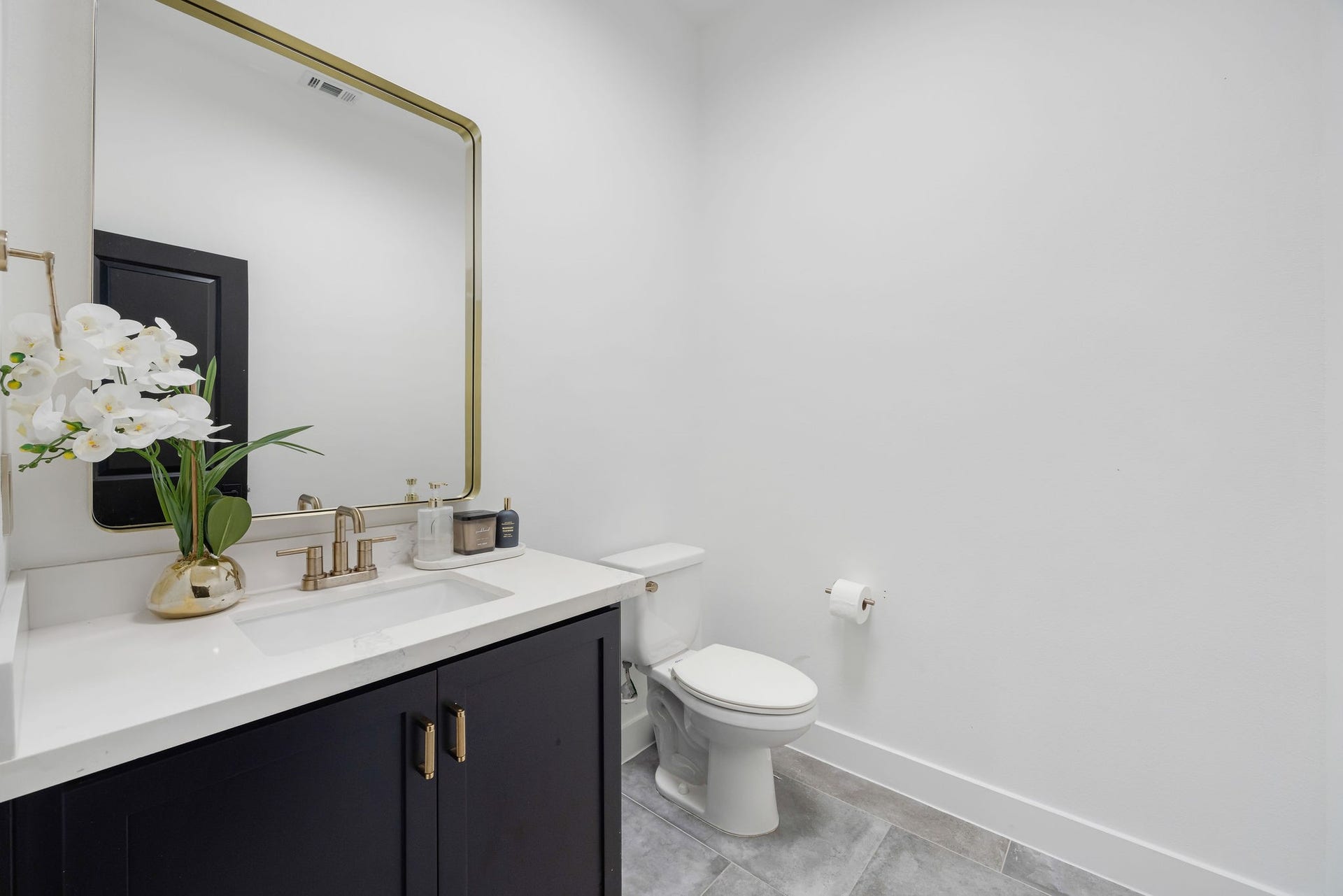 5537 Petty Street, Houston, TX 77007 Elegant powder room featuring a sleek black vanity with a white countertop, complemented by a large gold-framed mirror and contemporary fixtures.