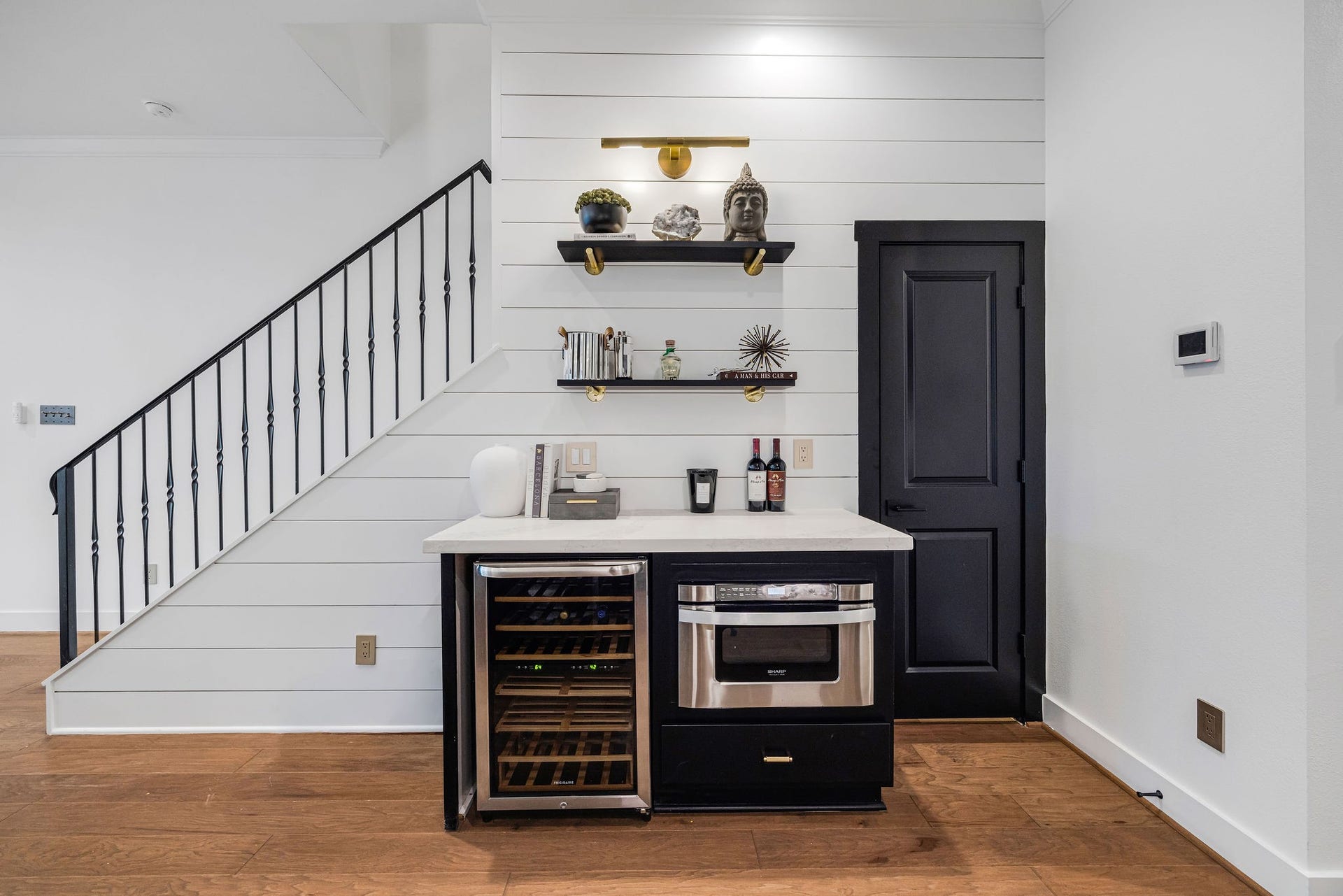 5537 Petty Street, Houston, TX 77007 Charming mini bar area under the staircase with sleek black cabinetry, a wine cooler, and stylish open shelving, offering a sophisticated touch to the living space.