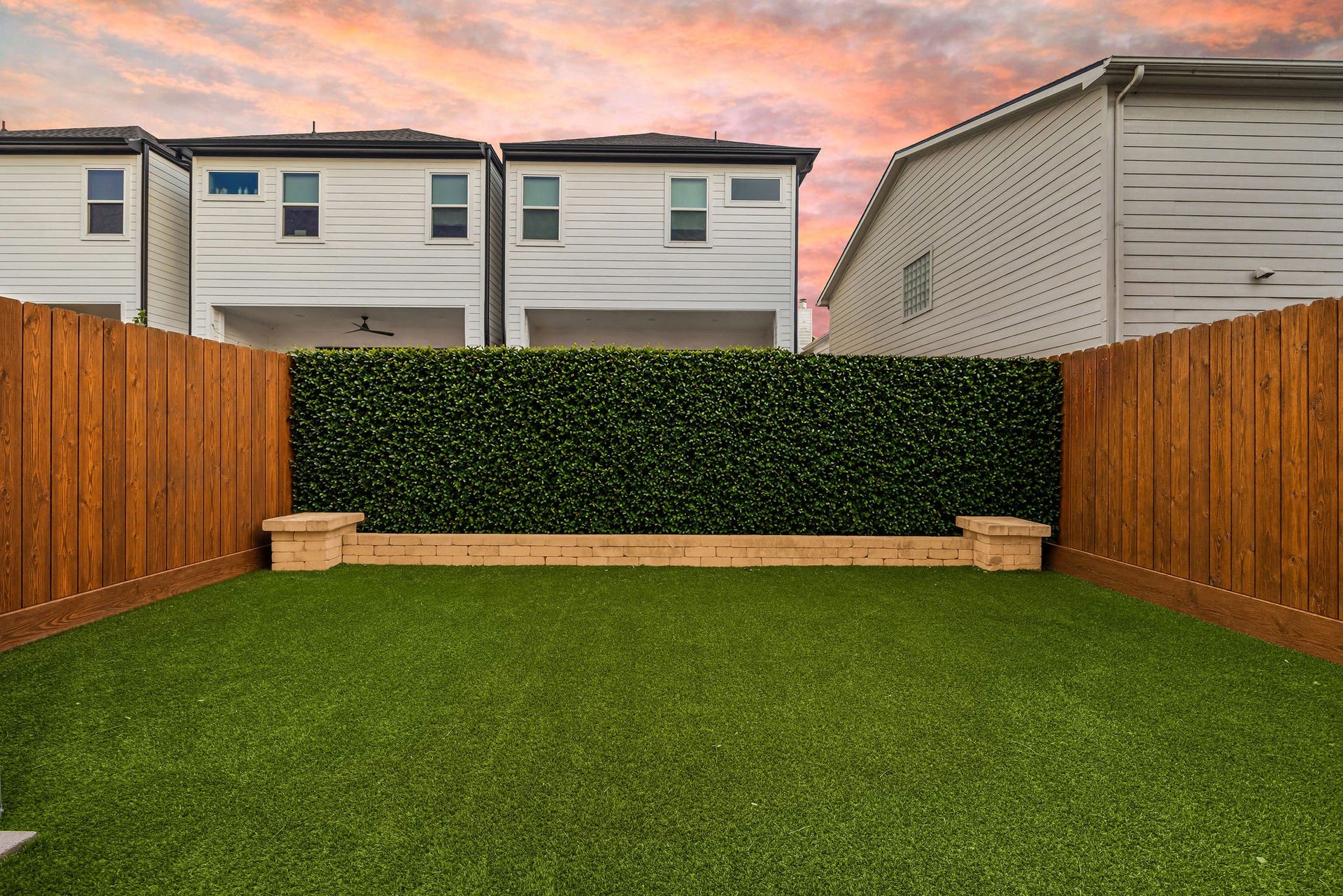5537 Petty Street, Houston, TX 77007 A serene backyard oasis features a lush artificial lawn surrounded by a wooden privacy fence and a backdrop of greenery, perfect for relaxation or entertaining.
