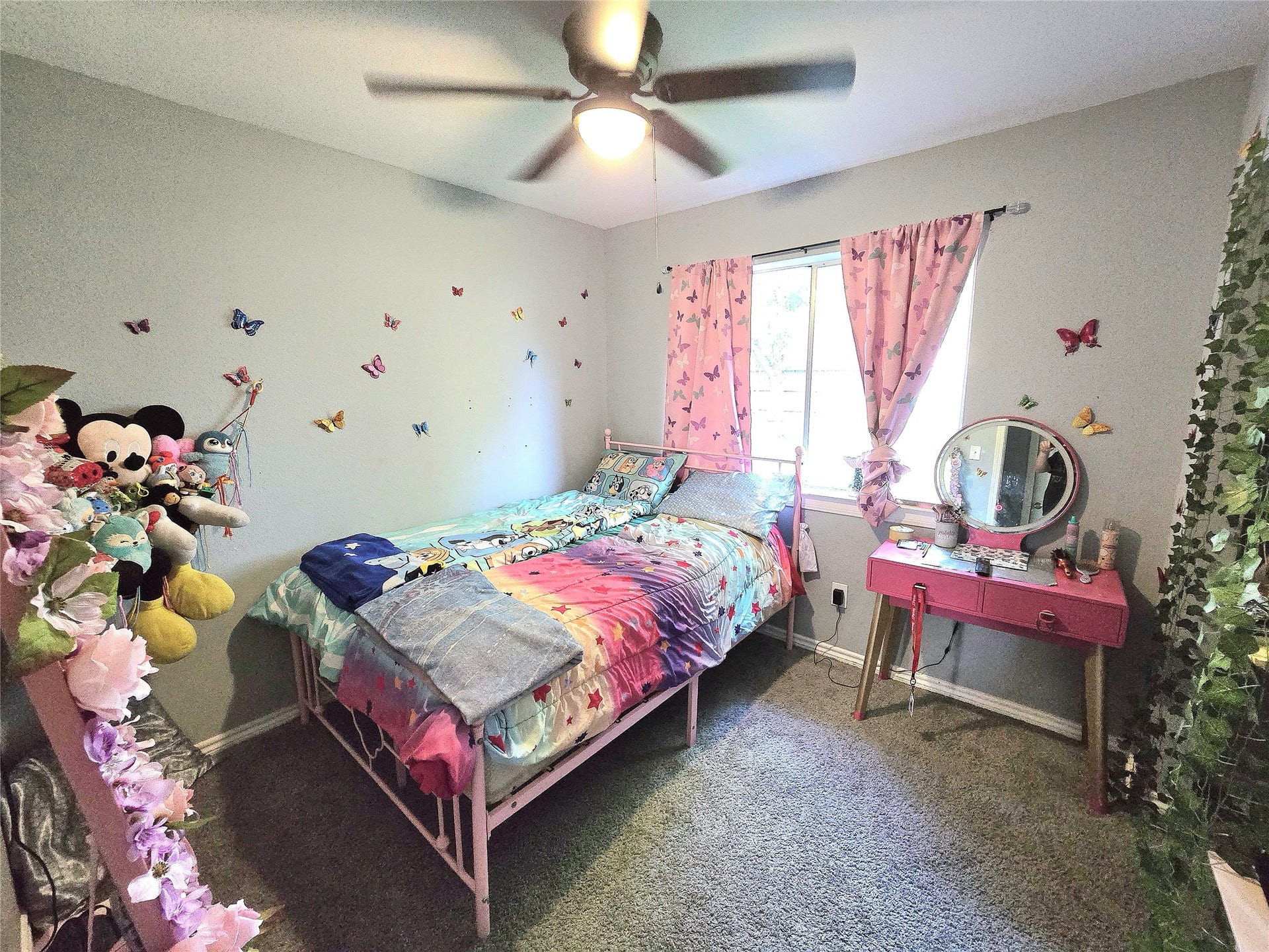5205 Winding Brook Drive, Dickinson, TX 77539 Charming bedroom with vibrant decor, featuring butterfly wall accents and a cozy bed, complemented by a vanity and a window for natural light.