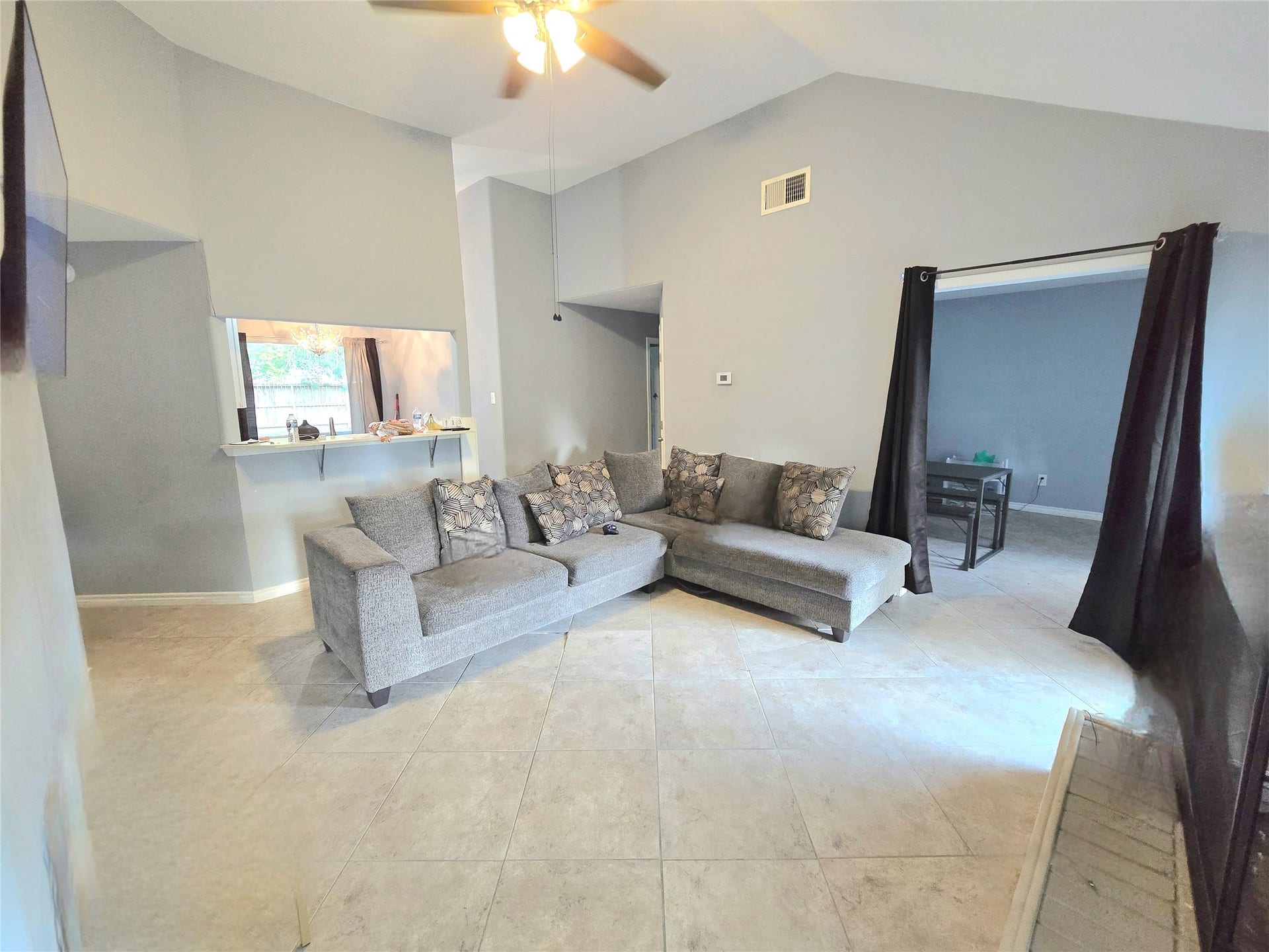 5205 Winding Brook Drive, Dickinson, TX 77539 Spacious living area with high ceilings and neutral tones features a cozy sectional sofa, tile flooring, and a convenient pass-through to the kitchen.