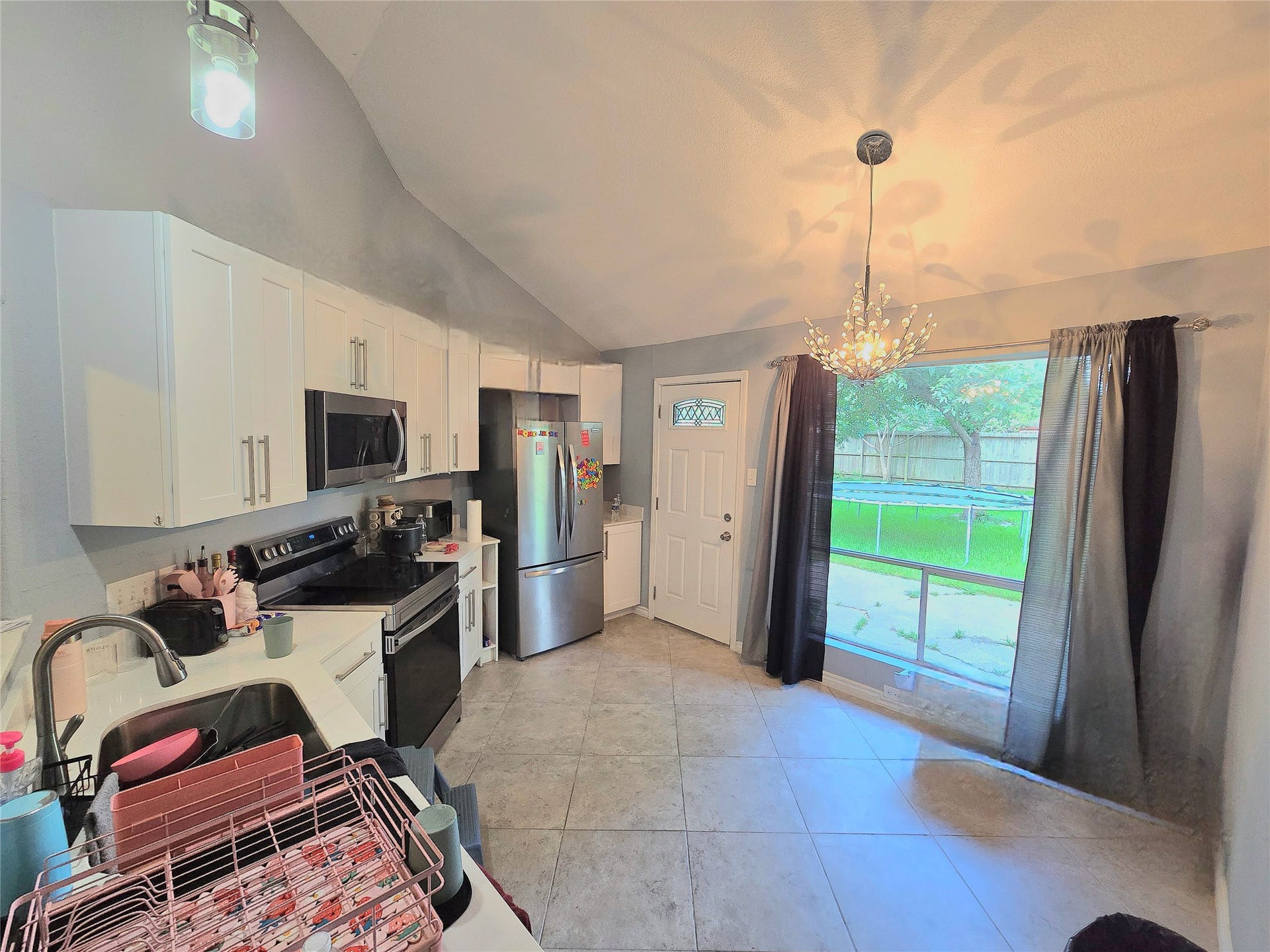 5205 Winding Brook Drive, Dickinson, TX 77539 Bright kitchen features modern appliances, sleek cabinetry, and a stylish chandelier, with a view of the backyard through large windows.