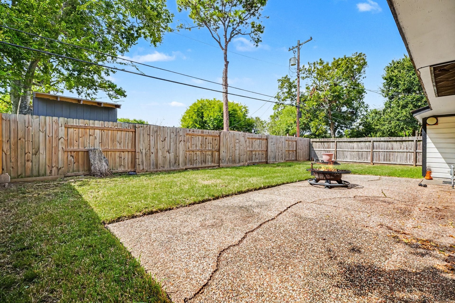 1317 N Natchez Drive, Texas City, TX 77591 Spacious backyard with a blend of grassy and paved areas, perfect for outdoor gatherings, enclosed by a tall wooden fence for privacy.