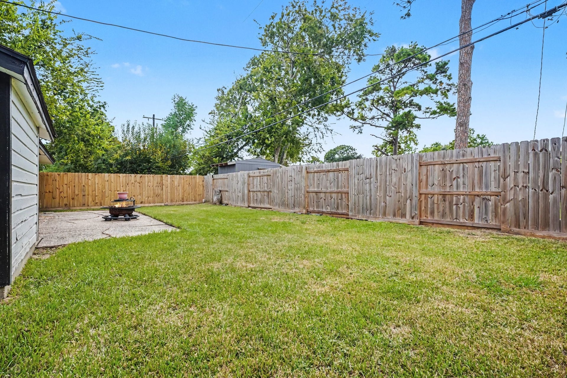 1317 N Natchez Drive, Texas City, TX 77591 Spacious backyard featuring a lush lawn, privacy fence, and a cozy fire pit area, perfect for outdoor gatherings.