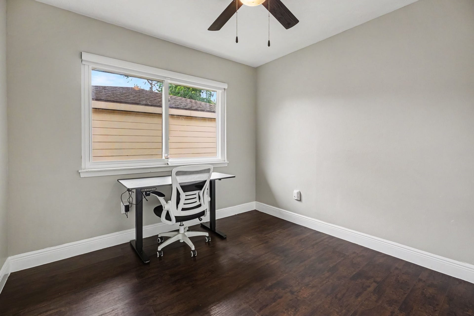 1317 N Natchez Drive, Texas City, TX 77591 Bedroom Two featuring a large window, sleek desk, comfortable chair, and stylish ceiling fan, all set against rich laminate flooring.