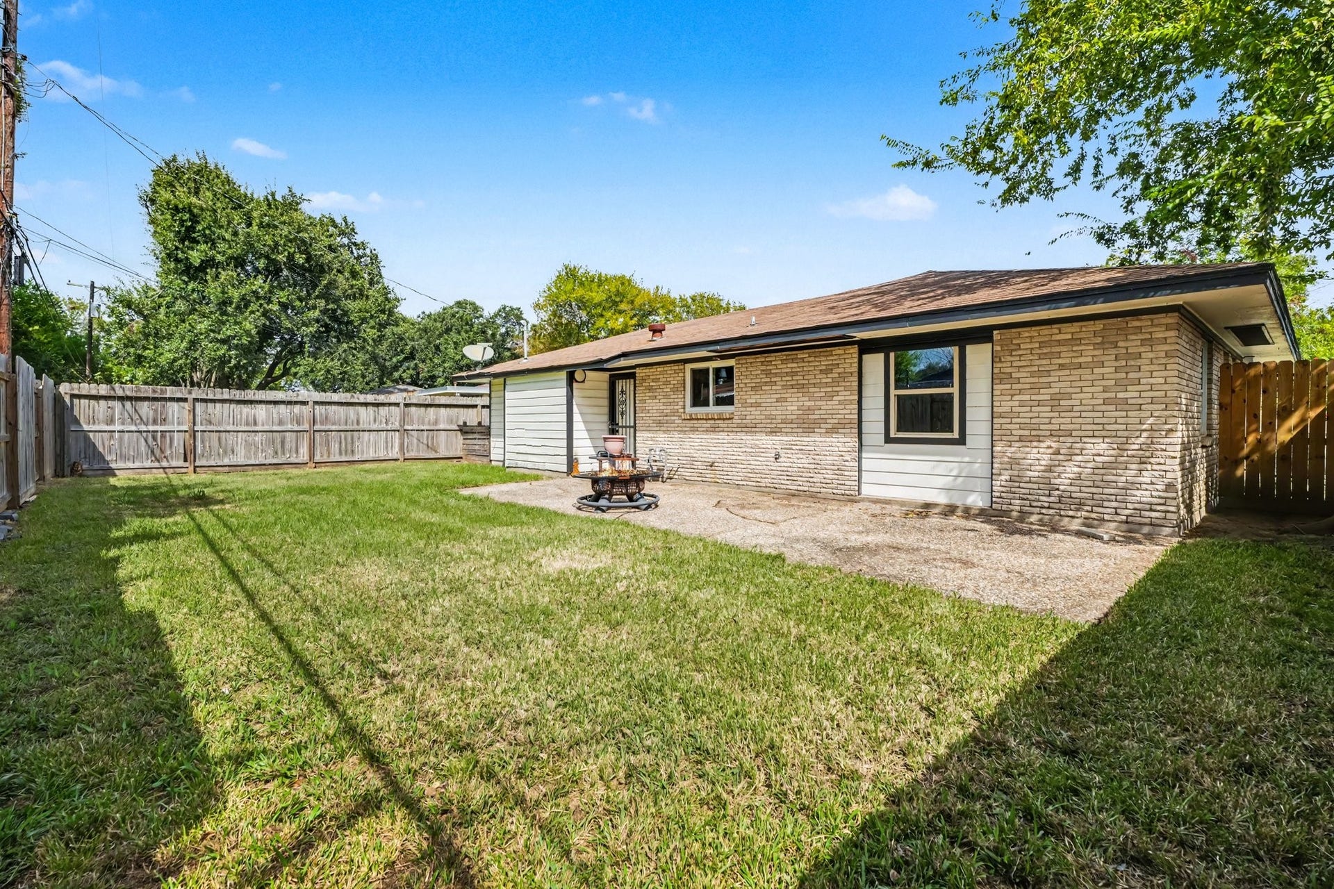 1317 N Natchez Drive, Texas City, TX 77591 Spacious backyard with a mix of lush grass and a paved patio, perfect for outdoor activities and relaxation, bordered by a sturdy wooden fence for privacy.