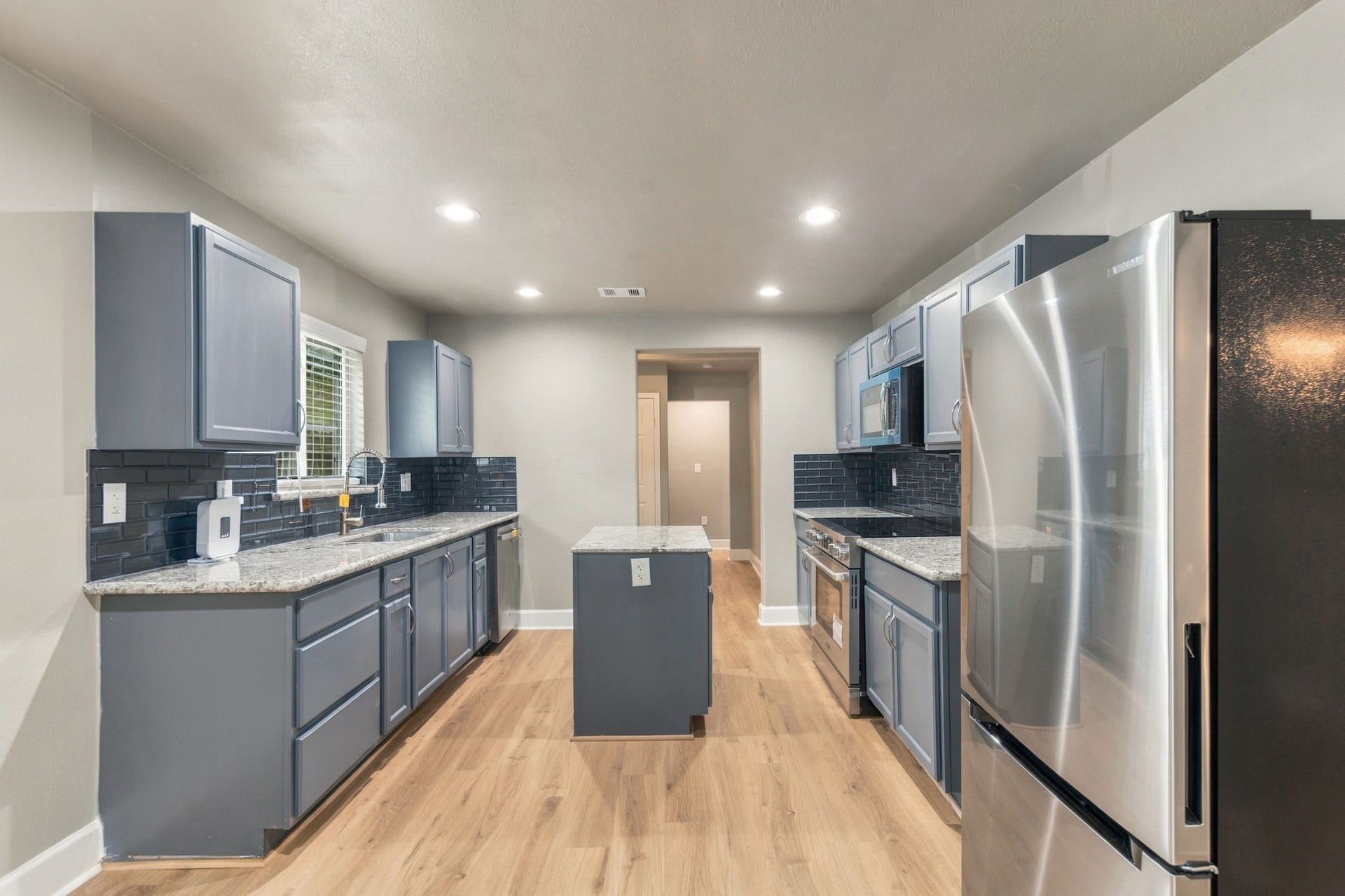 4637 Larkspur Street, Houston, TX 77051 Modern kitchen with sleek stainless steel appliances, elegant granite countertops, and stylish gray cabinets complemented by a chic dark tile backsplash.