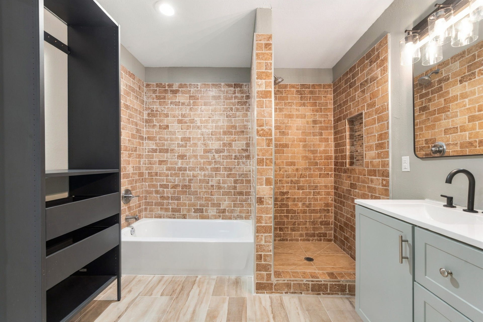 4637 Larkspur Street, Houston, TX 77051 Elegant bathroom featuring a spacious walk-in shower with rustic brick tiles, a modern bathtub, sleek vanity with a black faucet, and ample storage space.