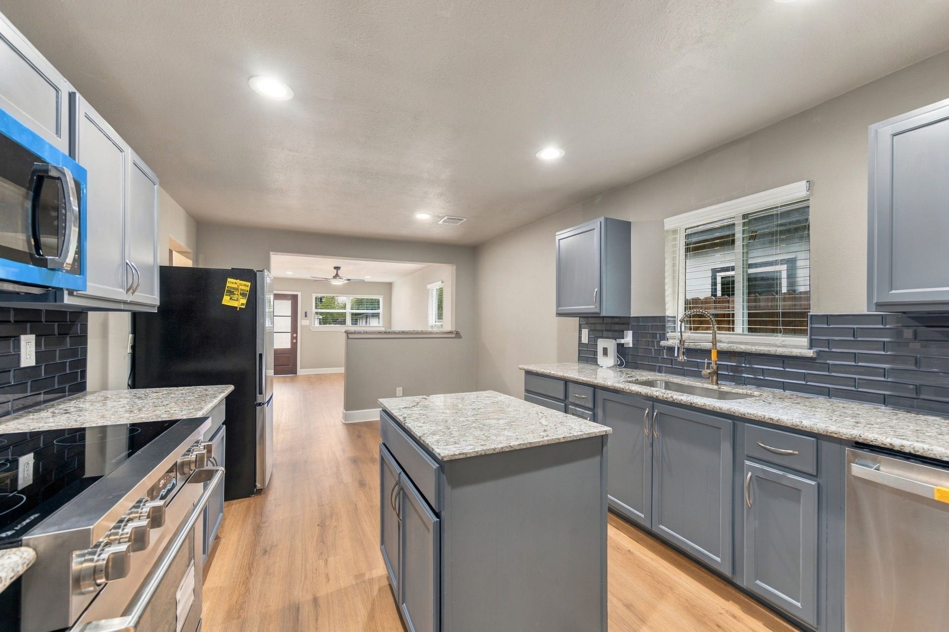 4637 Larkspur Street, Houston, TX 77051 Modern kitchen with sleek gray cabinets, granite countertops, and stainless steel appliances, opening to a bright living area with wood flooring.