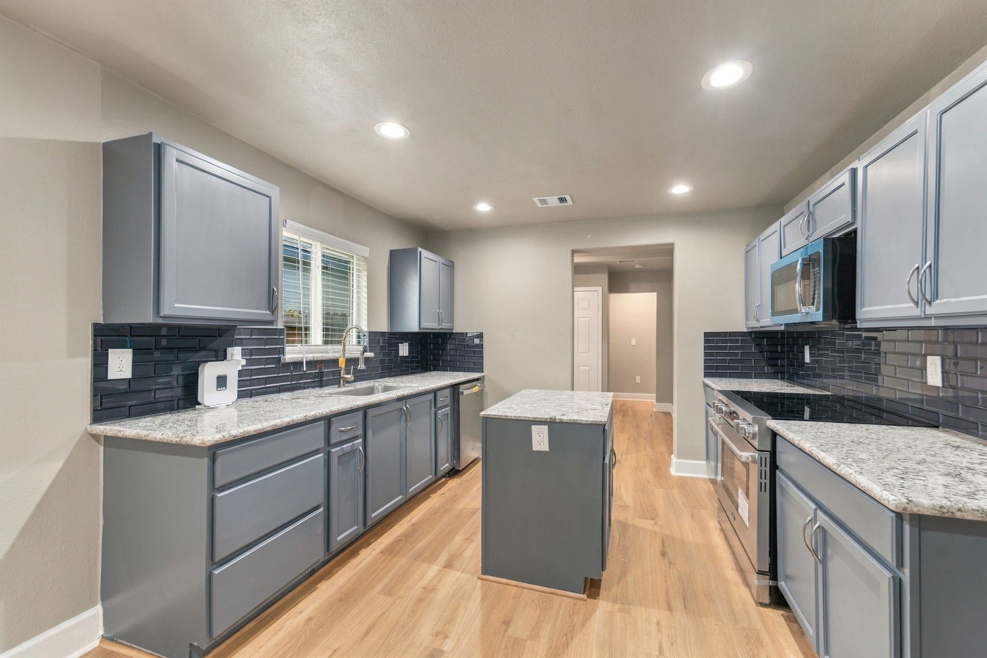 4637 Larkspur Street, Houston, TX 77051 Modern kitchen with sleek gray cabinets, granite countertops, and a stylish subway tile backsplash, complemented by stainless steel appliances and recessed lighting.