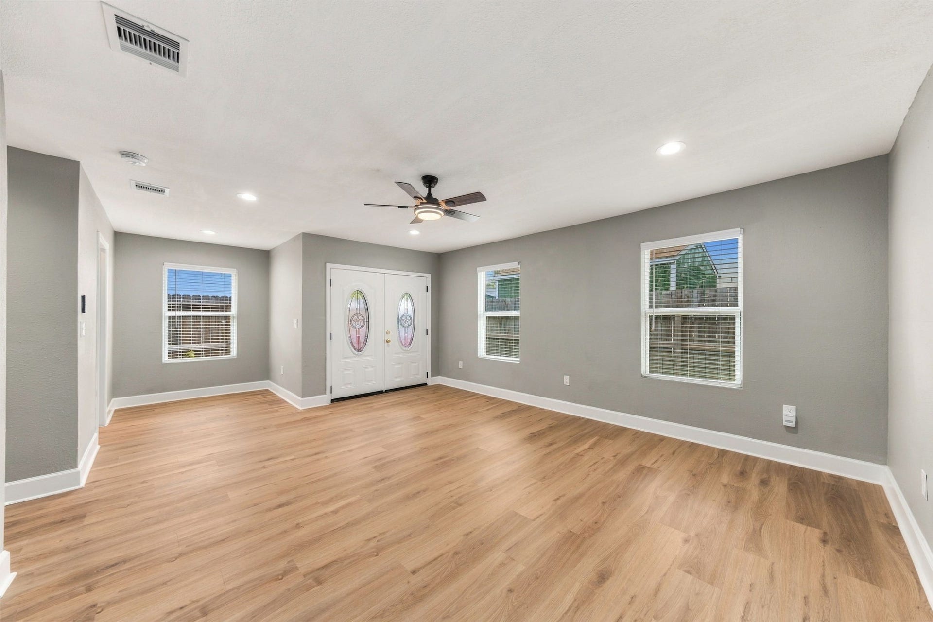 4637 Larkspur Street, Houston, TX 77051 Spacious living area with elegant wood flooring, neutral walls, and abundant natural light from multiple windows, featuring a ceiling fan and stylish double-door entry.