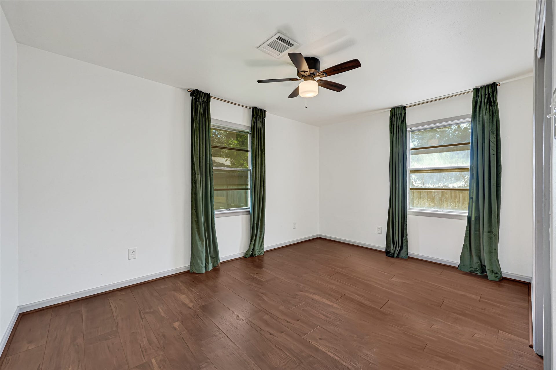 209 W 6th Street, Deer Park, TX 77536 Serene back bedroom featuring wood-look flooring, a ceiling fan, and natural light streaming through two large windows.
