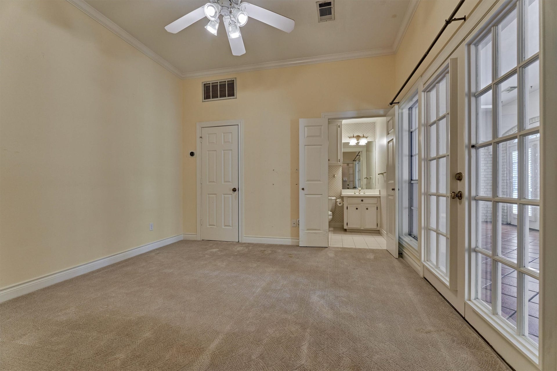 26 S Brokenfern Drive, The Woodlands, TX 77380 This downstairs bedroom has crown molding, a ceiling fan with lights, and plush carpet. A wall of divided-light French doors opens to the enclosed sunroom, and the ensuite full bath sits just inside the room with a white vanity, cabinet storage, and a tub or shower. A walk in closet adds generous storage. This is a flexible secondary suite that works well for guests or multigenerational living.