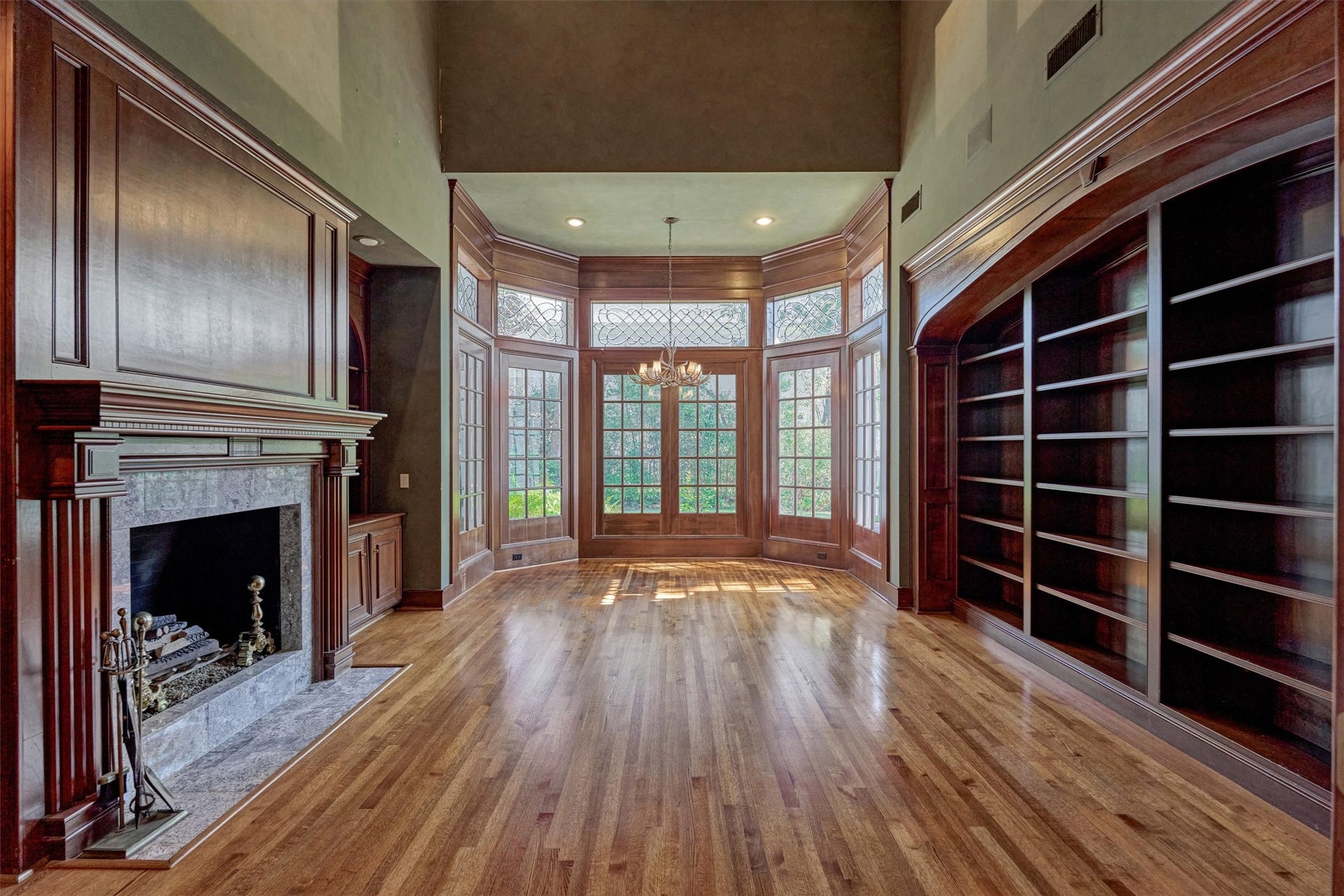 26 S Brokenfern Drive, The Woodlands, TX 77380 Picture a quiet evening by the fire in this two-story-ceiling library. Floor-to-ceiling cabinetry, a classic wood mantel with dentil molding, and a curved bay of mullioned French doors create an inviting, Ralph Lauren, old-world feel. Recessed lighting and an antler-style chandelier add warmth, and the garden views are a lovely backdrop. Use it as a music room, reading retreat, or executive-style home office.