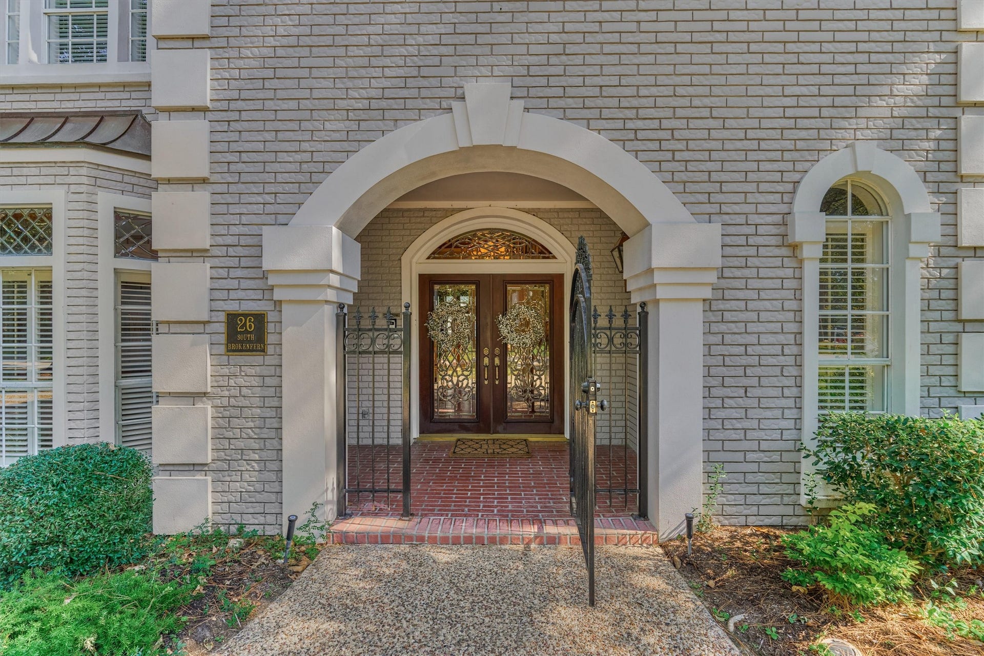 26 S Brokenfern Drive, The Woodlands, TX 77380 A grand stucco arch with a keystone-style accent frames the entry to this brick and stucco home. A wrought iron gate with scrollwork opens to a brick-paved porch and double mahogany-toned doors with beveled, decorative iron glass, topped by an arched transom. An arched window with stucco surround and a lantern-style light complete the elegant first impression.