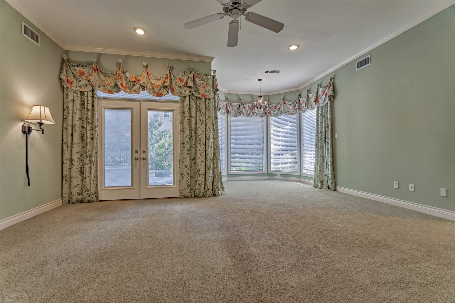 26 S Brokenfern Drive, The Woodlands, TX 77380 This Primary bedroom has 10-foot ceilings with deep crown molding, recessed lighting, and a ceiling fan. A bay of windows with a small chandelier makes a bright sitting or reading nook, and French doors with a transom open toward the outdoors. Plush carpet and generous proportions leave plenty of room for a king-size bed and a full seating area, and the room overlooks the backyard.