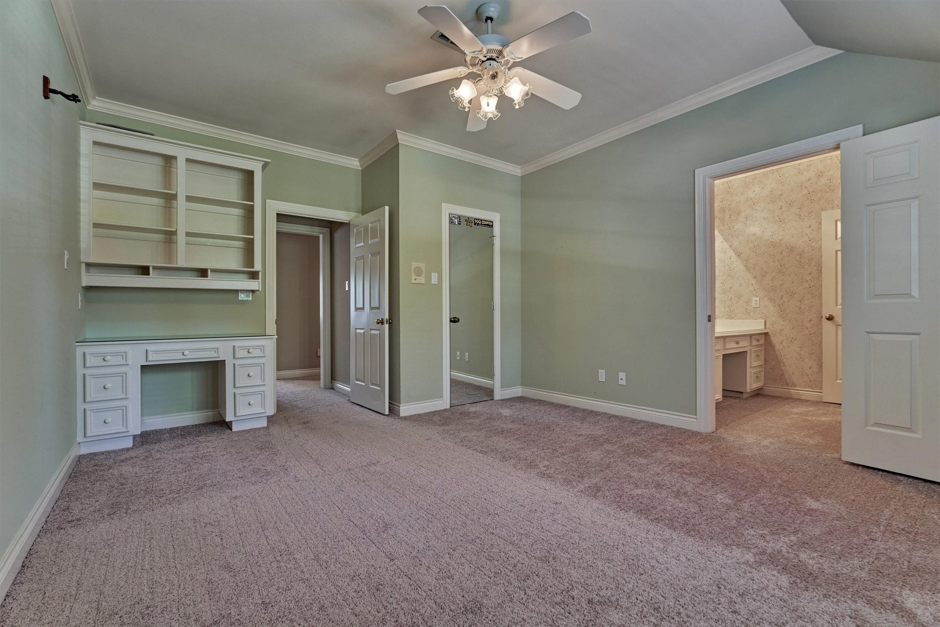 26 S Brokenfern Drive, The Woodlands, TX 77380 This second upstairs bedroom has a built-in desk with drawers and an upper hutch with open shelves and cubbies, perfect for homework or a computer station. Crown molding, a ceiling fan with lights, and a slightly vaulted ceiling line add detail, and plush carpet runs throughout. A closet with a mirrored door sits beside the desk area. The doorway on the right opens to this bedrooms private sink and counter area, which connects to the shared bath.