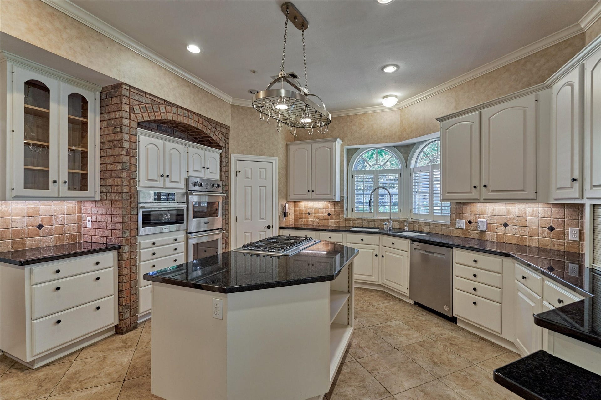 26 S Brokenfern Drive, The Woodlands, TX 77380 Another angle of this chefs kitchen highlights its bright, open layout. Under-cabinet lighting warms the granite countertops, and a shuttered window over the sink brings in views of the front yard. A walk-in pantry keeps everything organized, and the large island is perfect for prep, serving, or casual meals.