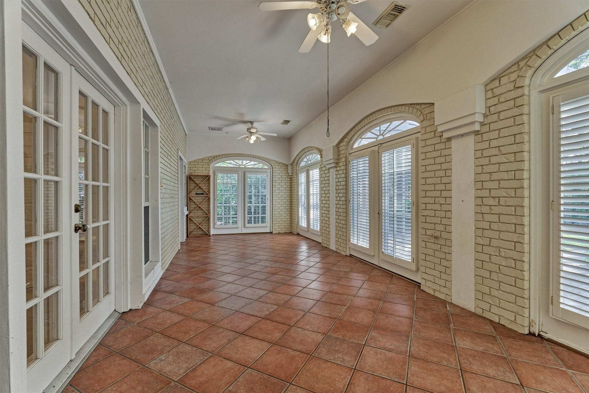 26 S Brokenfern Drive, The Woodlands, TX 77380 This enclosed sunroom, off the family room, is lined with painted brick walls and arched, transom-topped windows and French doors with plantation shutters. Warm terracotta tile floors are set on the diagonal, and a vaulted, curved ceiling with ceiling fans adds an airy feel. Two sets of double doors give easy access: one opens to the backyard, and the other leads to the secondary downstairs suite.