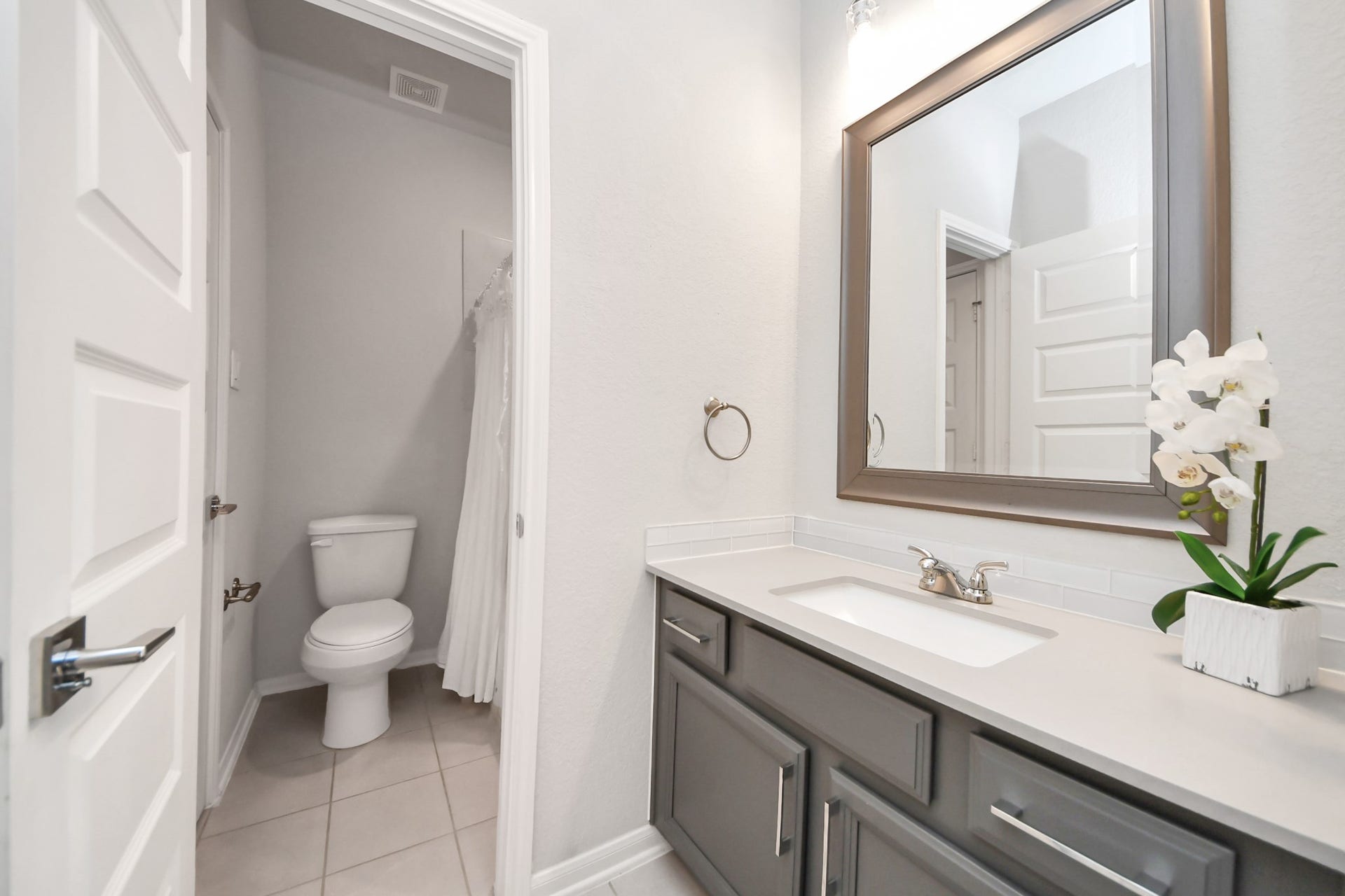 Elegant secondary bathroom featuring a sleek vanity with a large, framed mirror, stylish gray cabinetry, and a bright, contemporary design is off the secondary bedroom in previous picture.