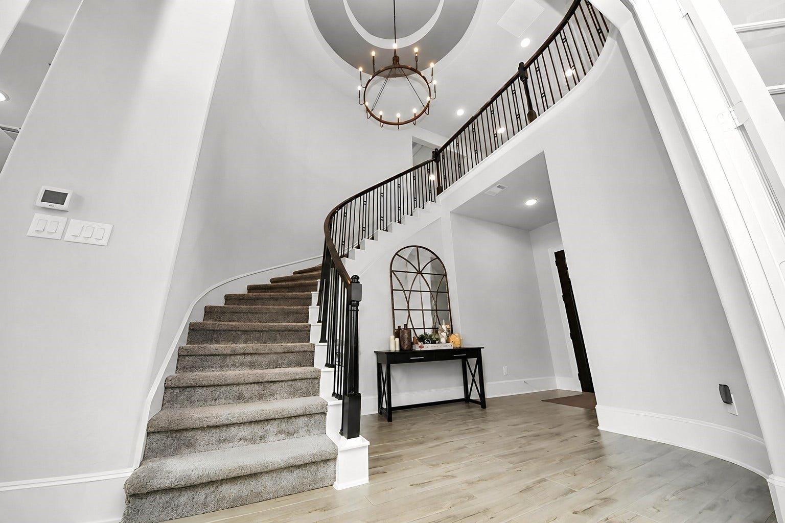 Elegant entryway featuring a grand curved staircase, complemented by a stylish chandelier and sleek wood look tile flooring.