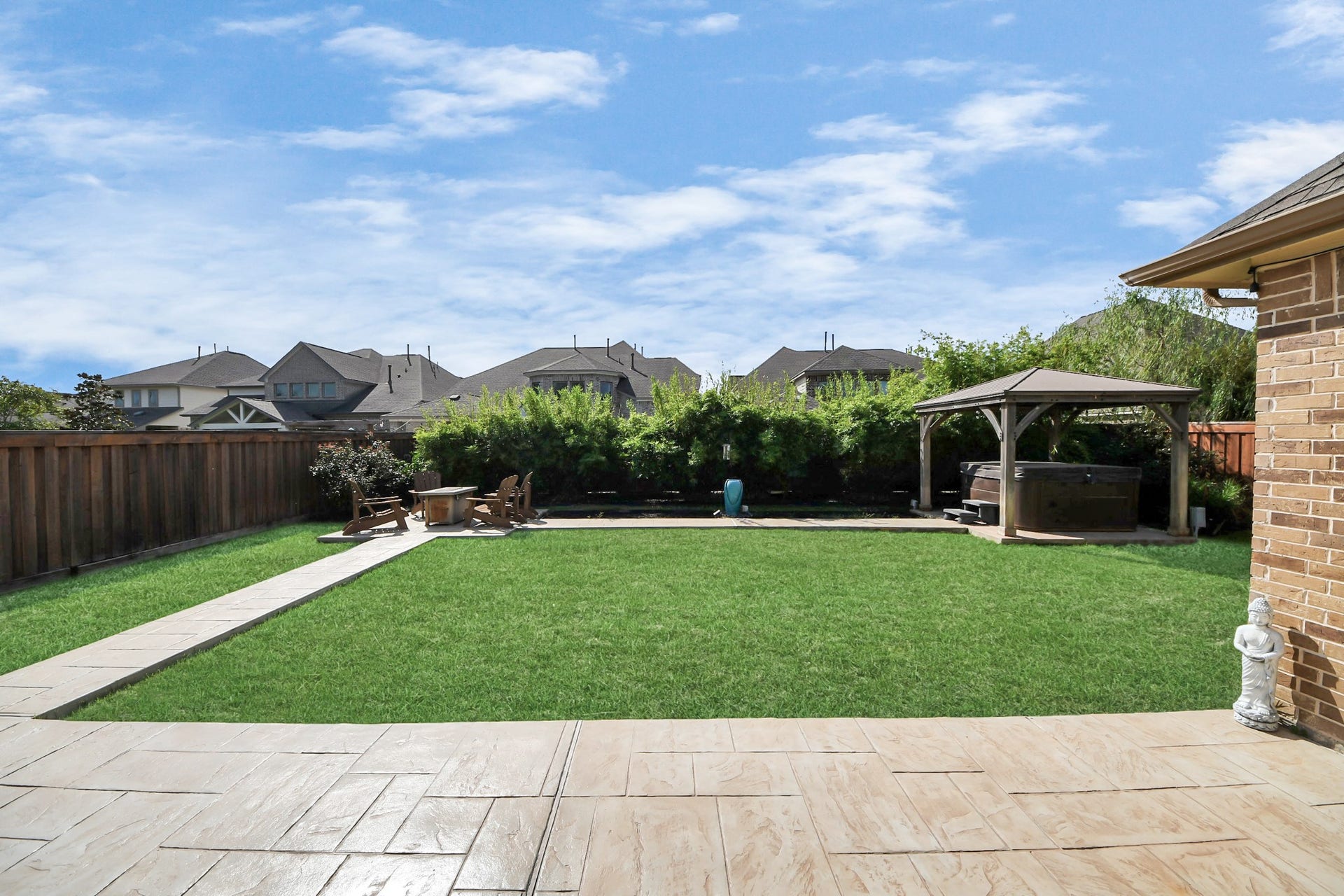 Spacious backyard featuring a lush green lawn, a stamped paved concrete patio, and a cozy pergola with seating, perfect for outdoor relaxation and entertaining.