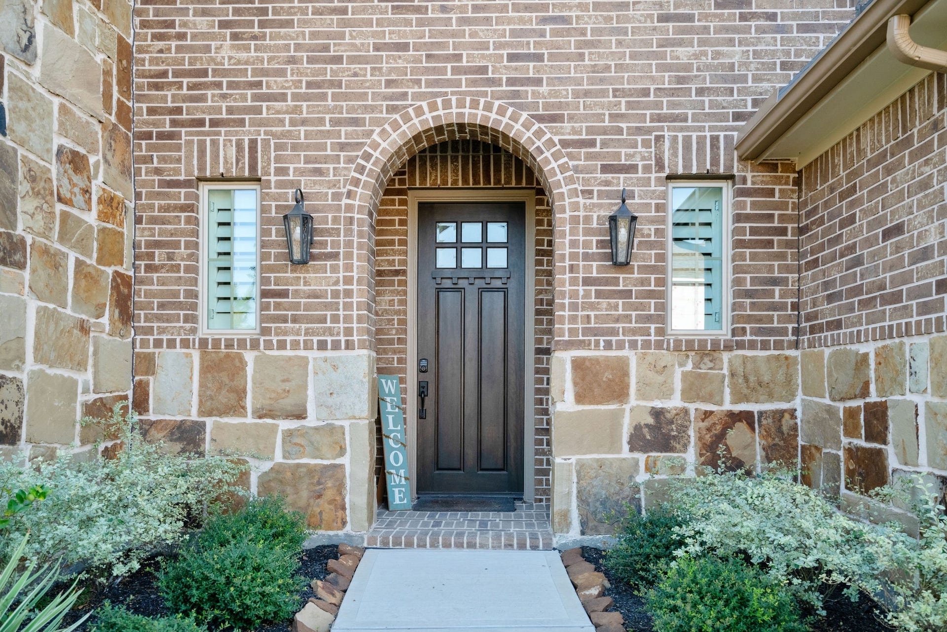Charming entryway featuring a stylish arched brick design with a welcoming front door flanked by elegant lantern-style lights.