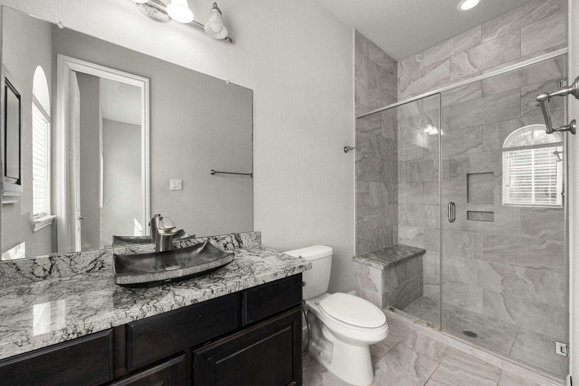10606 Comeaux Lane, Richmond, TX 77407 A private ensuite serves the downstairs secondary bedroom, featuring a vessel sink, striking counters, and a walk-in glass shower with a built-in bench.