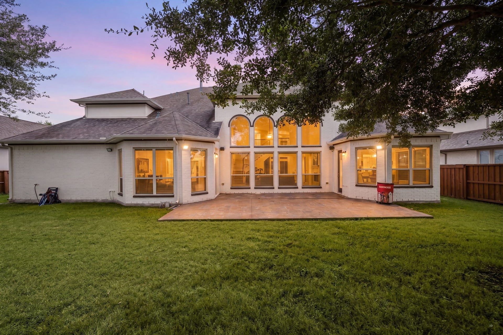 10606 Comeaux Lane, Richmond, TX 77407 At dusk, the home's dramatic arched two-story windows glow from within, overlooking a covered patio and expansive backyard framed by mature trees.