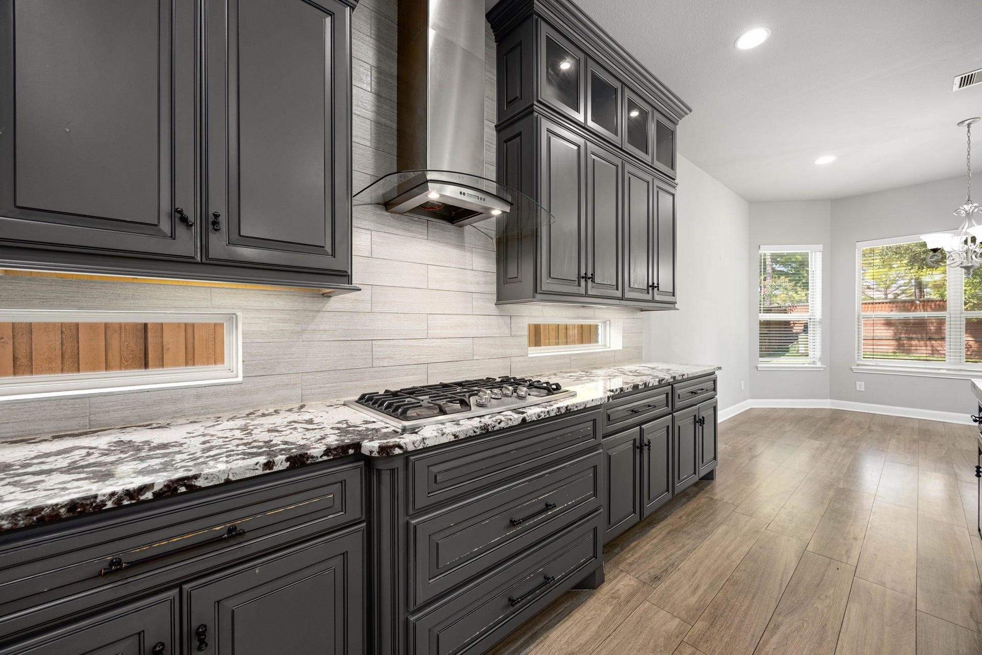 10606 Comeaux Lane, Richmond, TX 77407 A gas cooktop beneath a sleek glass-and-steel range hood anchors this section of the kitchen, framed by marble counters and a tile backsplash that extends throughout the space.