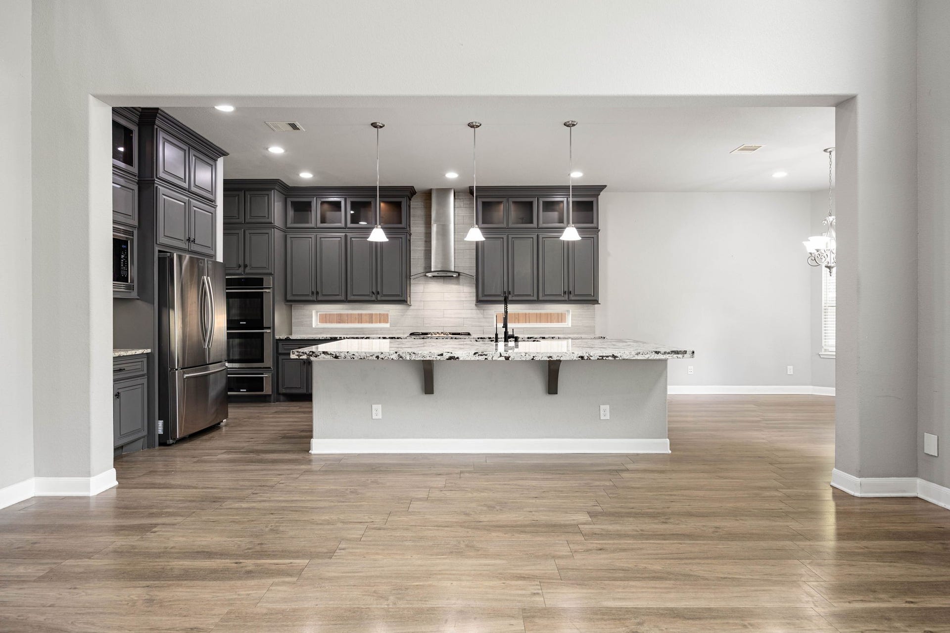 10606 Comeaux Lane, Richmond, TX 77407 Rich dark cabinetry and a stainless steel hood vent frame this open-concept kitchen, where a large center island with pendant lighting and granite counters flows seamlessly into the main living space.