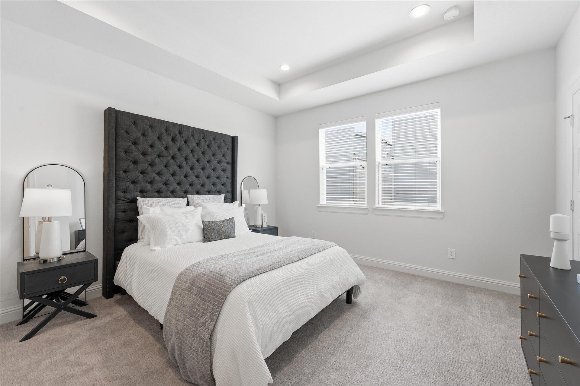 Discover serene comfort in this elegant primary bedroom, where a plush bed with a striking tufted headboard is beautifully illuminated by natural light from ample windows.