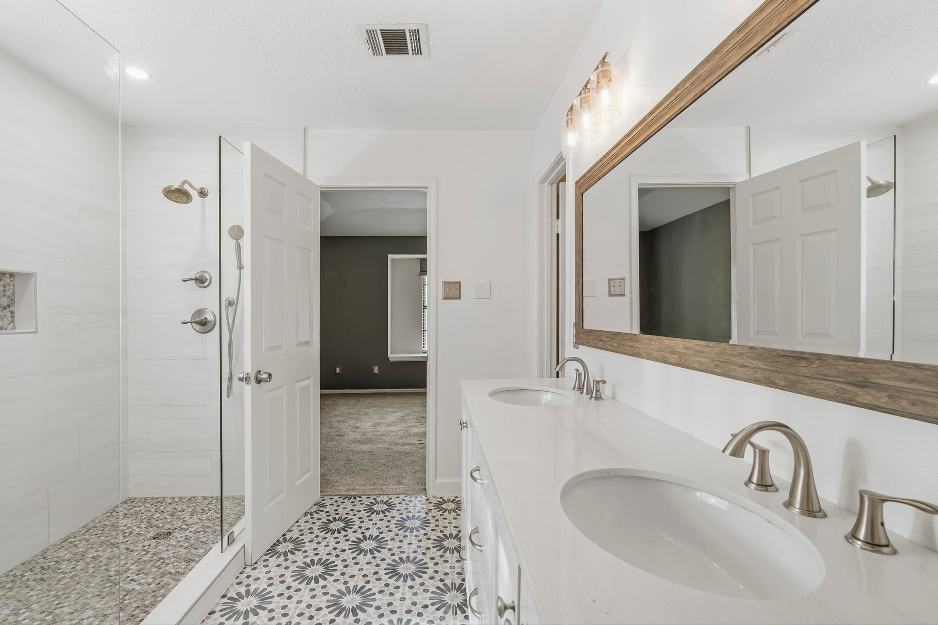 3311 Richmond Ferry Court, Richmond, TX 77406 The walk-in shower offers a frameless glass enclosure, large-format tile, pebble-style flooring, and a rainfall showerhead with handheld fixture. Eye-catching patterned tile flooring adds character, while bright neutral finishes create a fresh, modern feel.