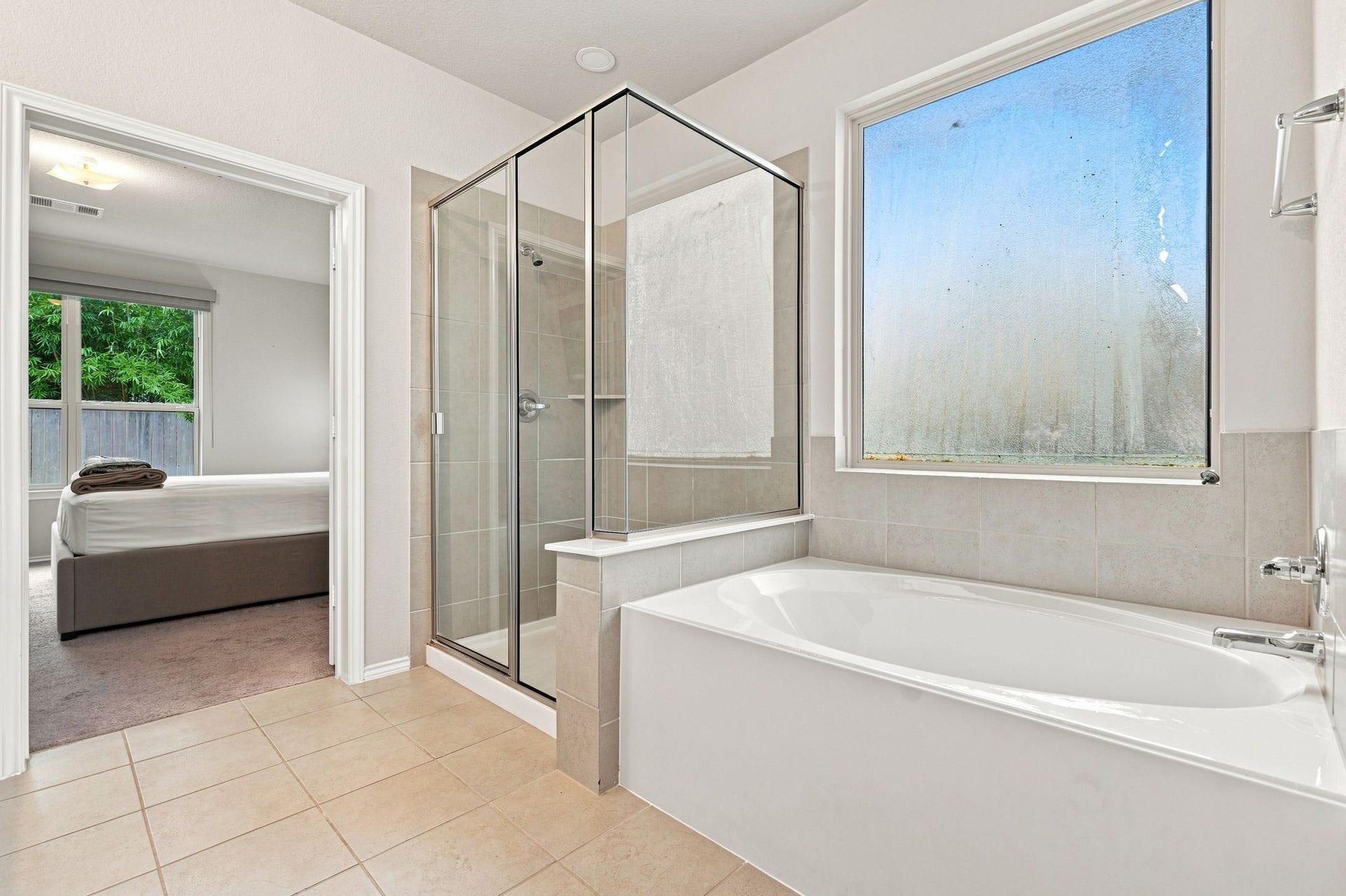 2307 Northern Great White Court, Katy, TX 77449 This primary bathroom features a standalone glass-enclosed shower stall alongside a deep soaking tub set against neutral tile surrounds.