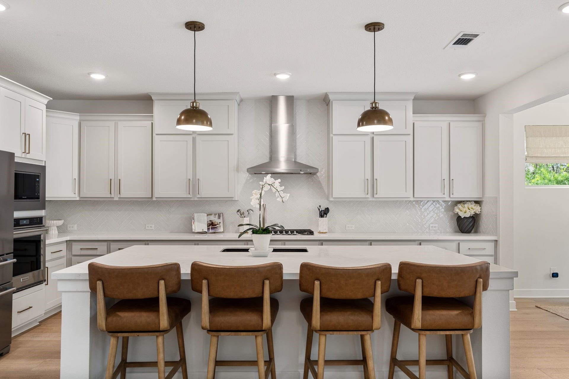 Oversized quartz island w/seating for four, abundant cabinetry, elegant herringbone tile backsplash, designer pendant lighting, and beautiful wood flooring.