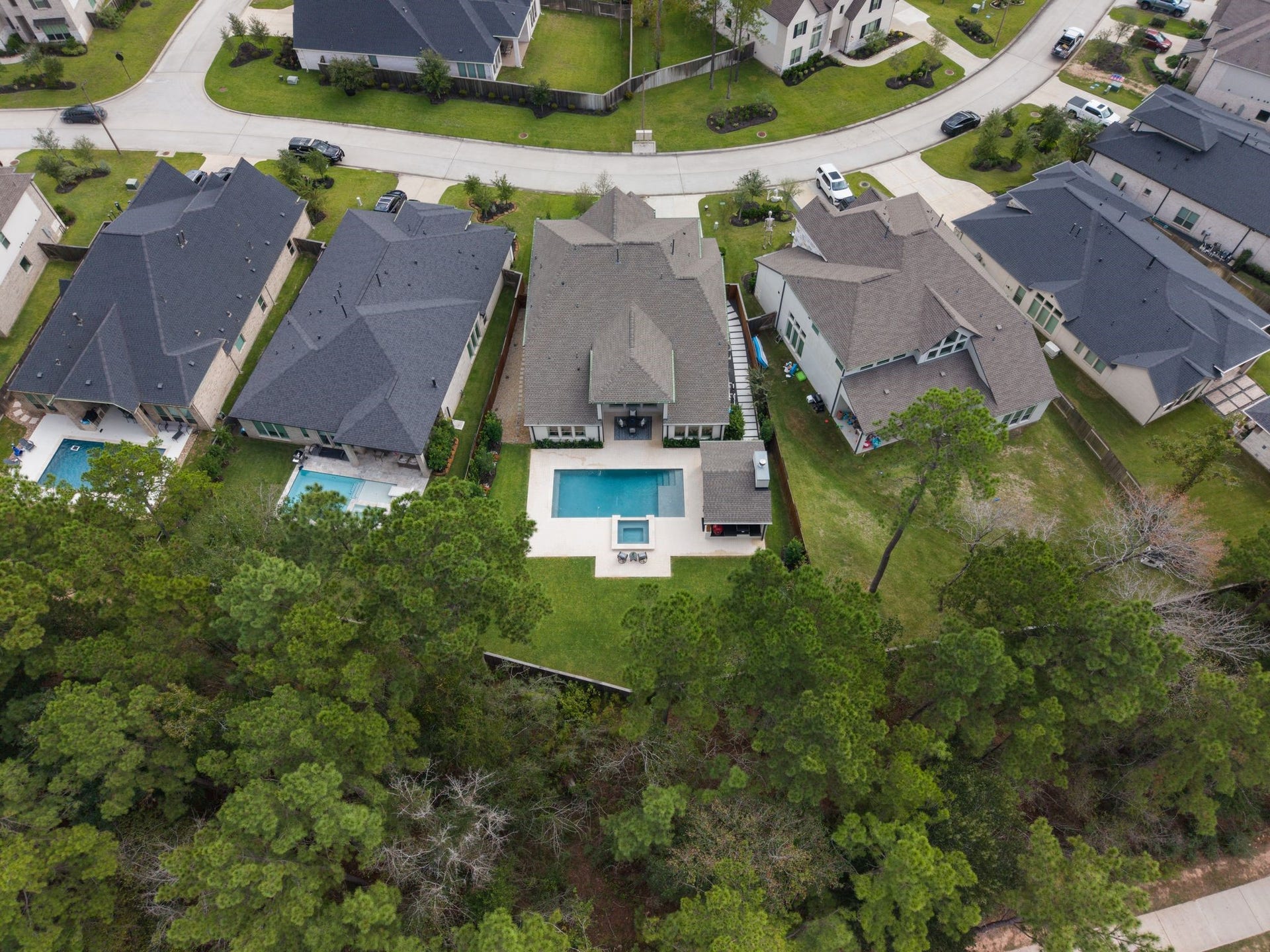Impressive aerial view highlights the privacy provided by the wooded greenbelt, an unusually spacious backyard with abundant lawn space beyond the resort-style pool and cabana, and beautifully designed, low-maintenance side yards featuring extensive custom hardscapingoffering the perfect blend of luxury, privacy, and effortless outdoor living!