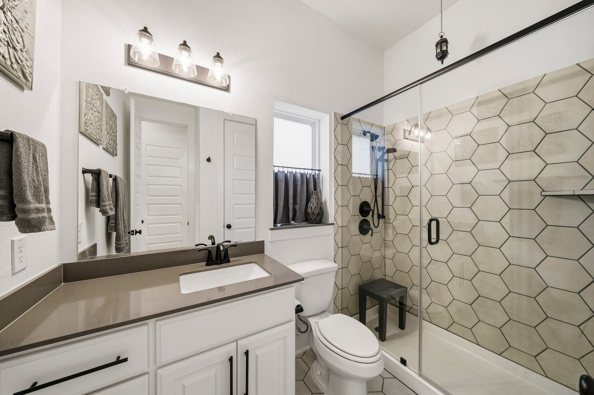 2514 Heritage Park Drive, Missouri City, TX 77459 The Next-Gen ensuite bath is beautifully appointed with designer tile flooring, a Quartz-topped vanity with mirror and lighting above and a frameless glass shower featuring a striking hexagonal tile surround, shower head and separate handheld spray wand.