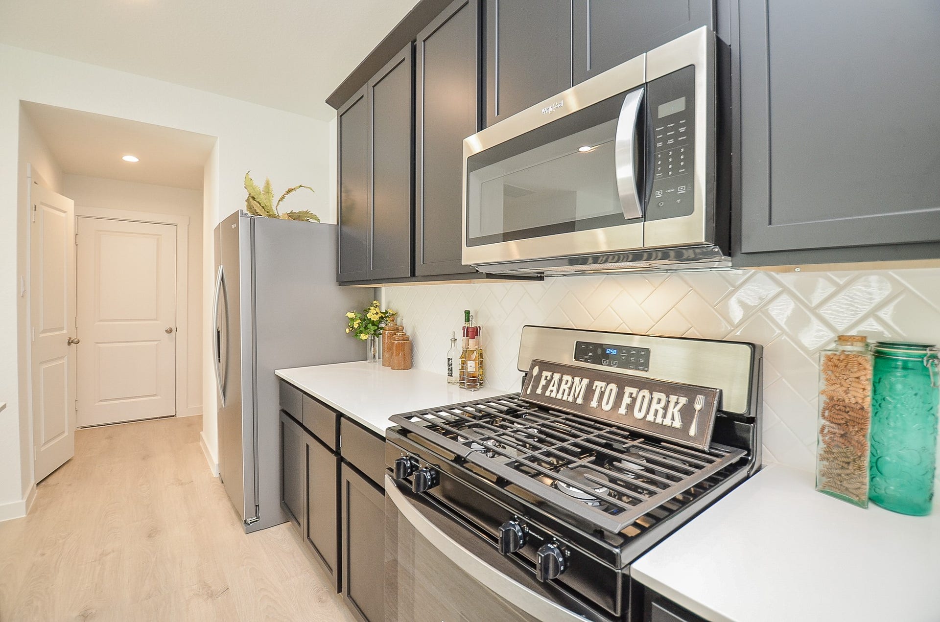 7814 Bel Fiore Drive, Richmond, TX 77406 Modern kitchen featuring sleek stainless steel appliances, elegant dark cabinetry, and a stylish herringbone backsplash.