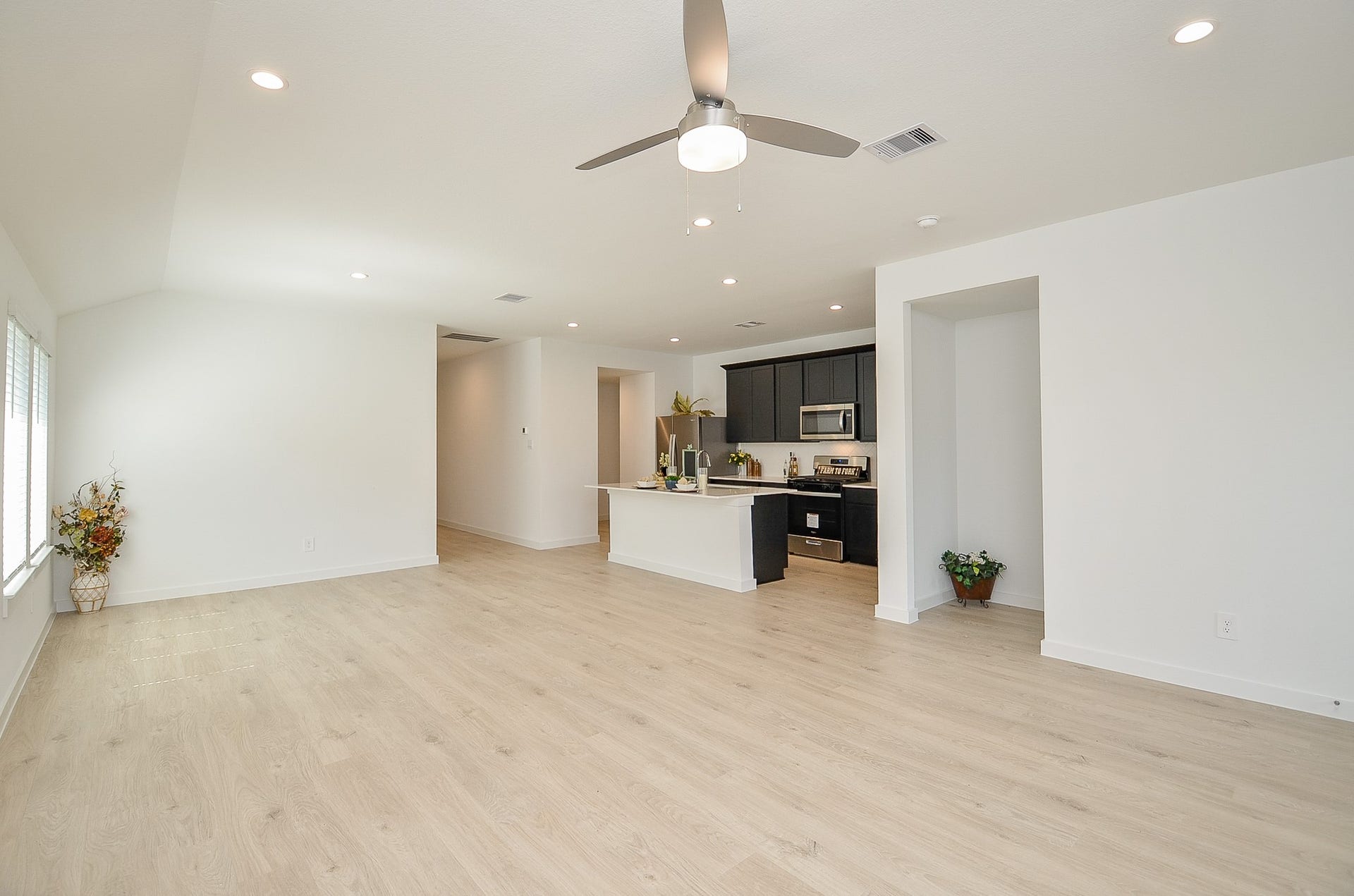 7814 Bel Fiore Drive, Richmond, TX 77406 Spacious open-concept living area with modern light wood floors, recessed lighting, and a sleek kitchen featuring dark cabinetry and stainless steel appliances.