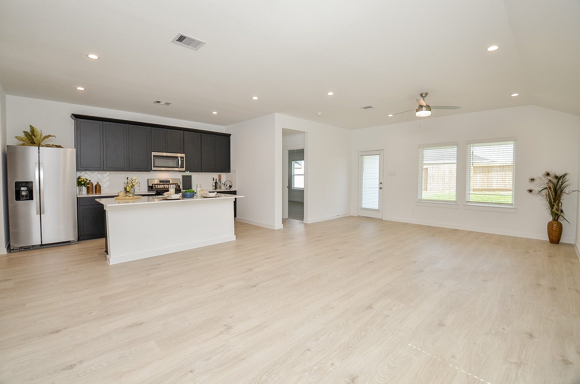 7814 Bel Fiore Drive, Richmond, TX 77406 Spacious open-concept living area featuring sleek hardwood floors, a modern kitchen with dark cabinetry and stainless steel appliances, and ample natural light from large windows.